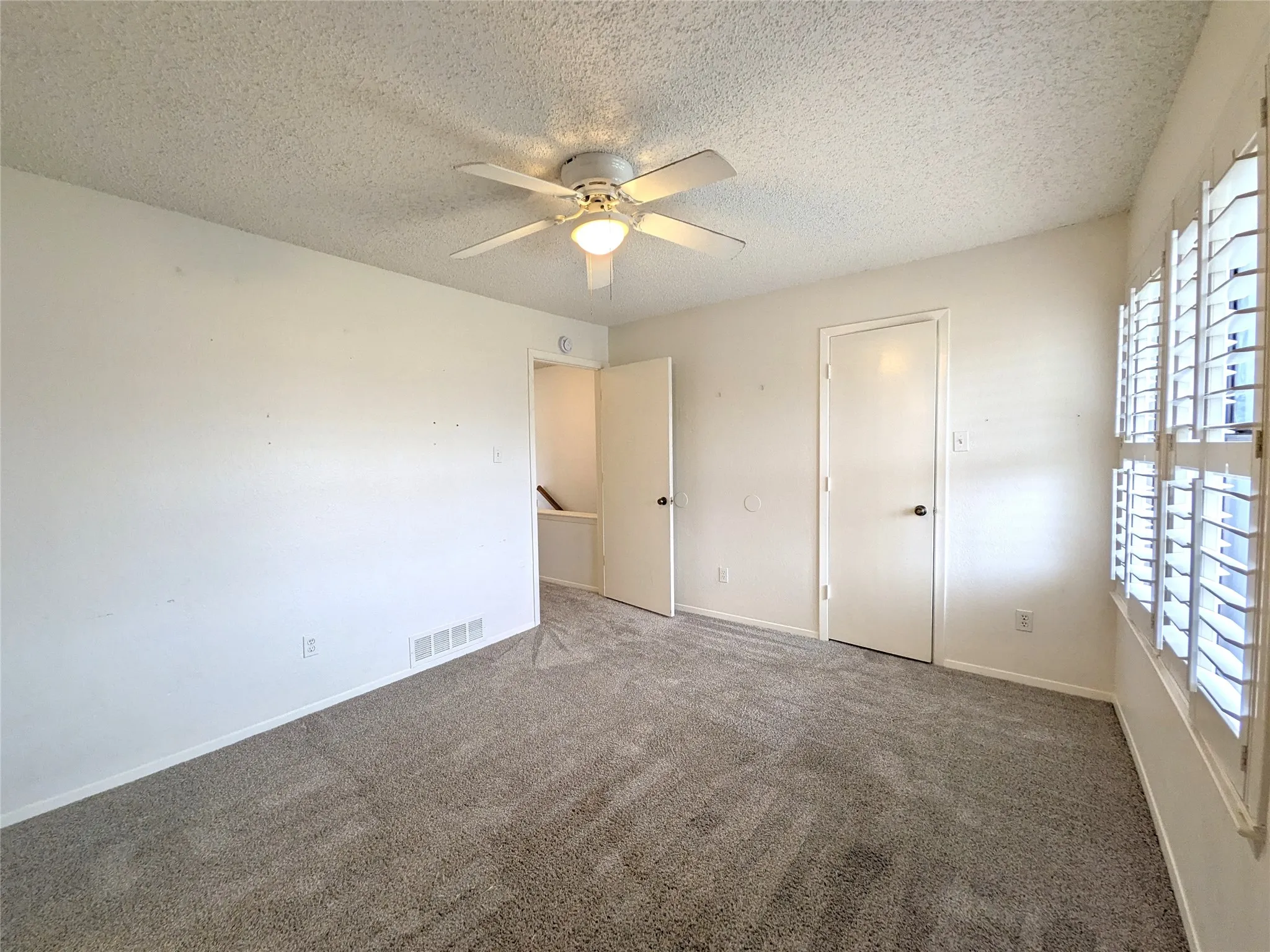 Carpeted interior space featuring a ceiling fan with integrated lighting, window with white plantation shutters, and two solid panel doors with round black hardware