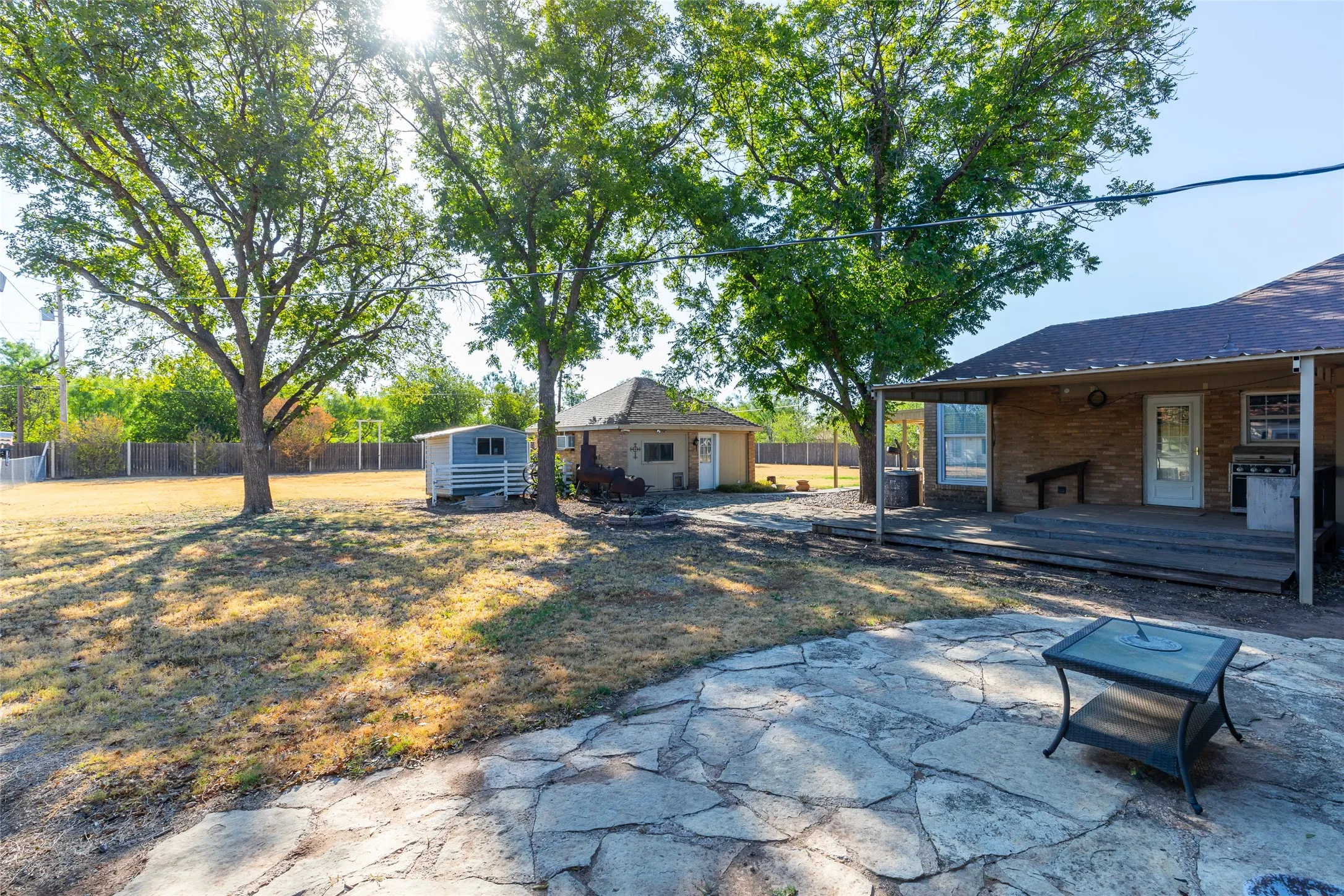 Expansive backyard with a large flagstone patio, covered wood deck, and mature trees