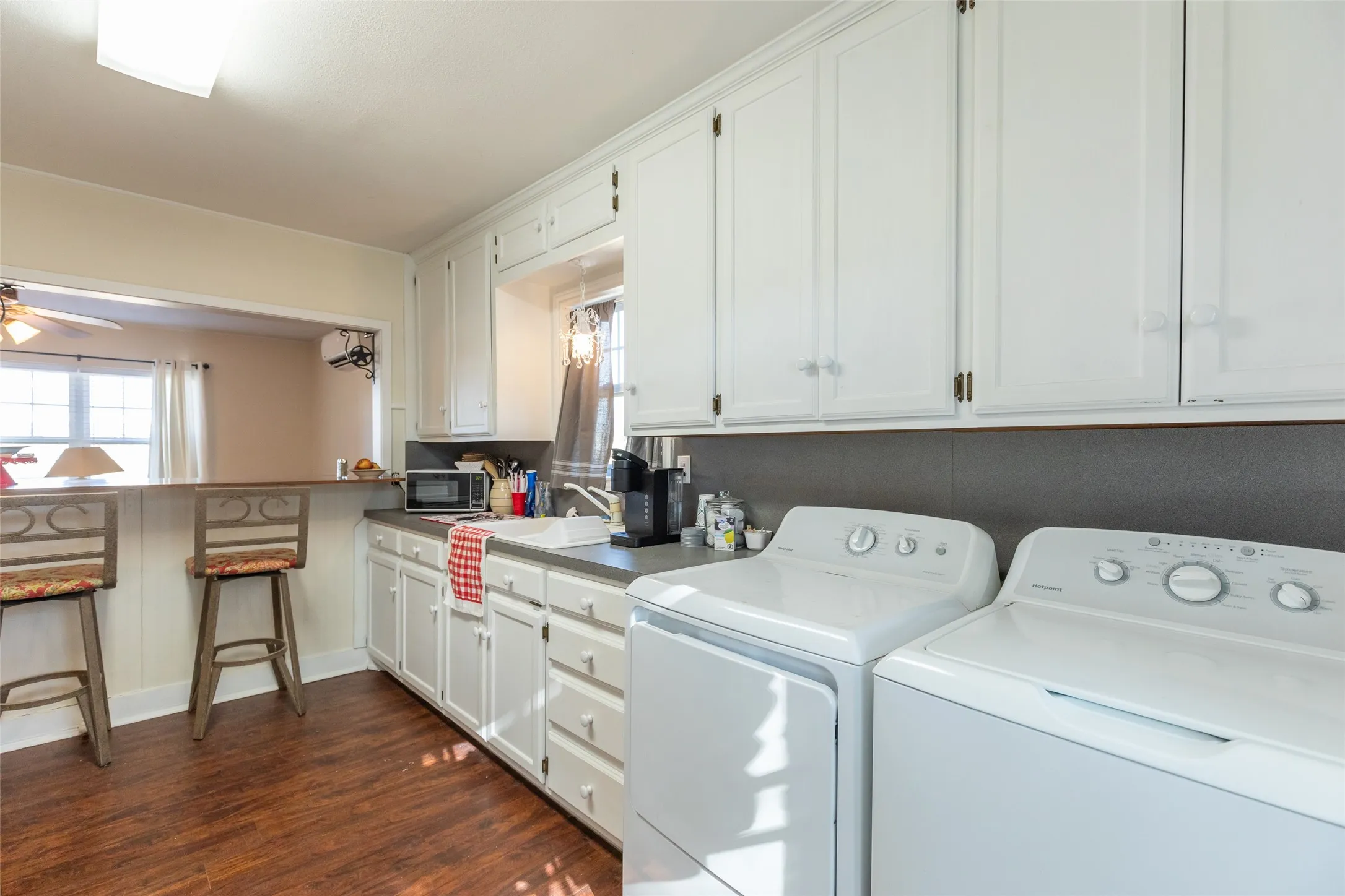 White cabinetry with clear knobs, wood-finish flooring, and a pass-through bar with seating
