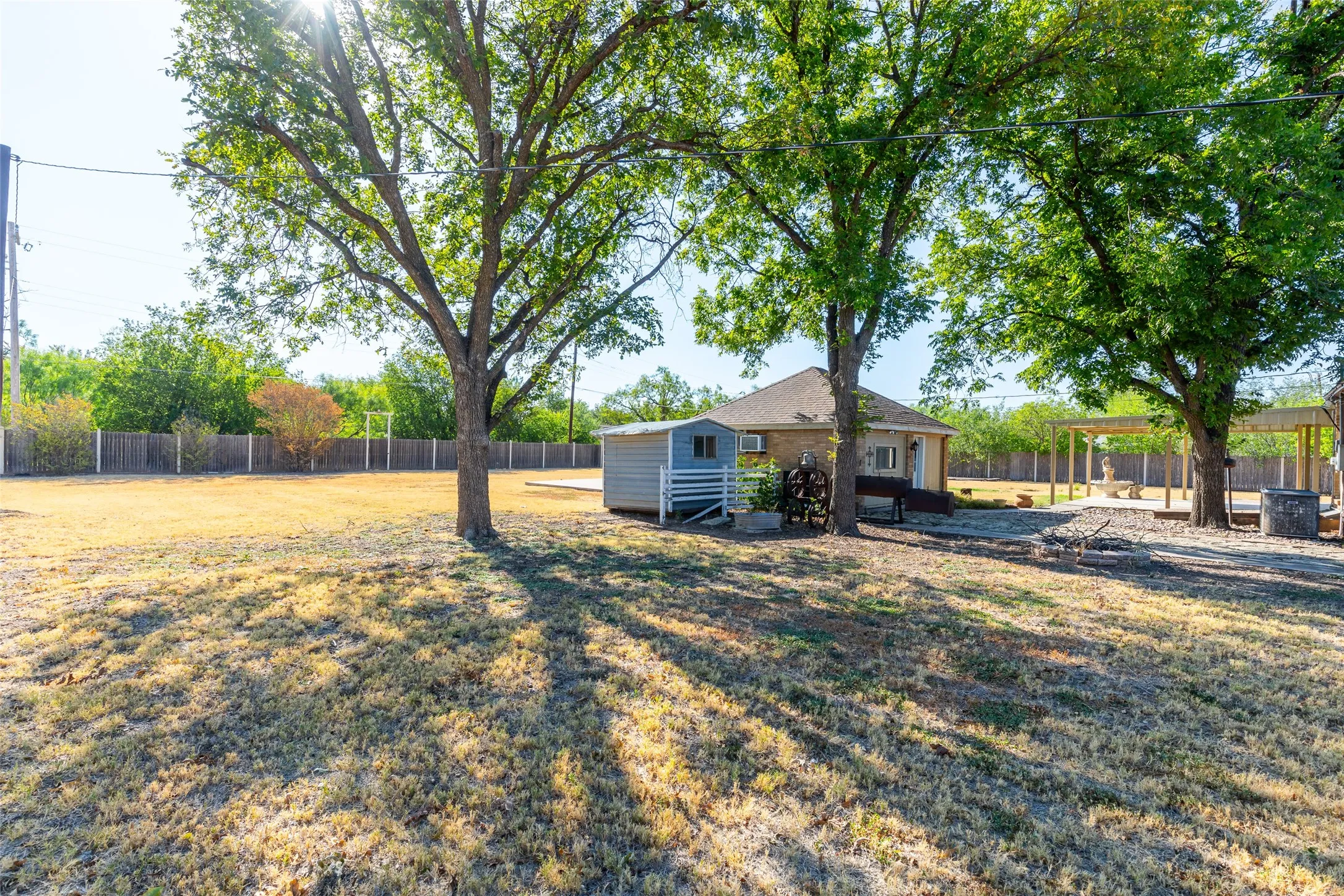 Expansive backyard featuring mature trees, a wooden privacy fence, a detached shed, a pergola, and a gravel patio area
