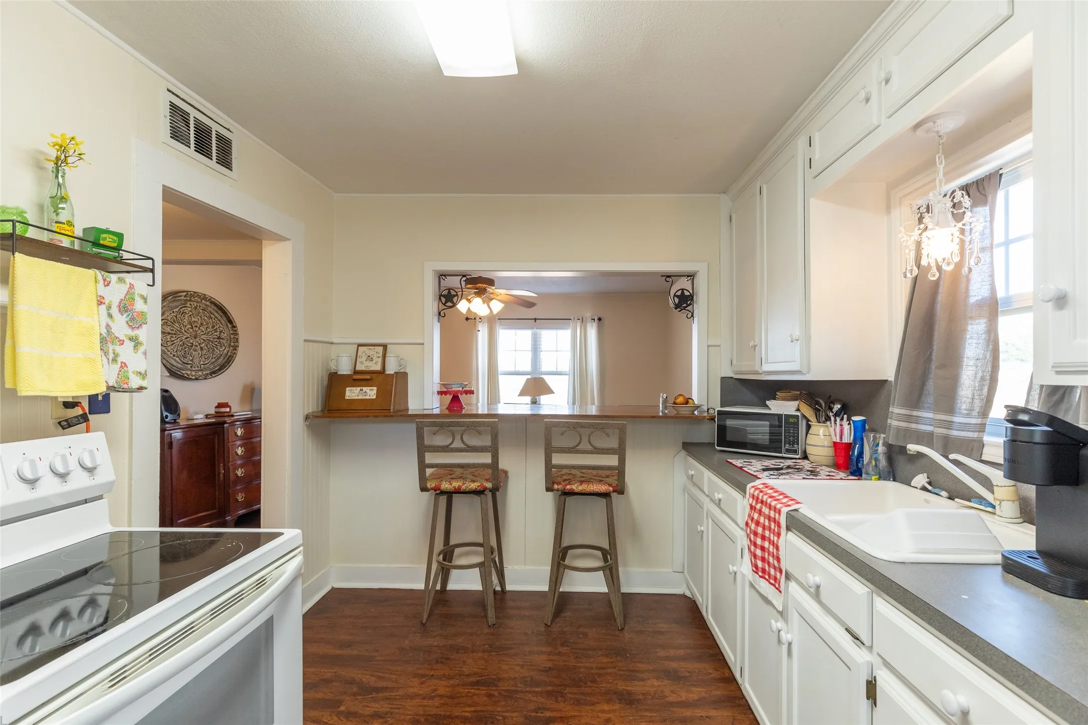 White cabinetry with dark countertops, wood-finish flooring, and a pass-through opening