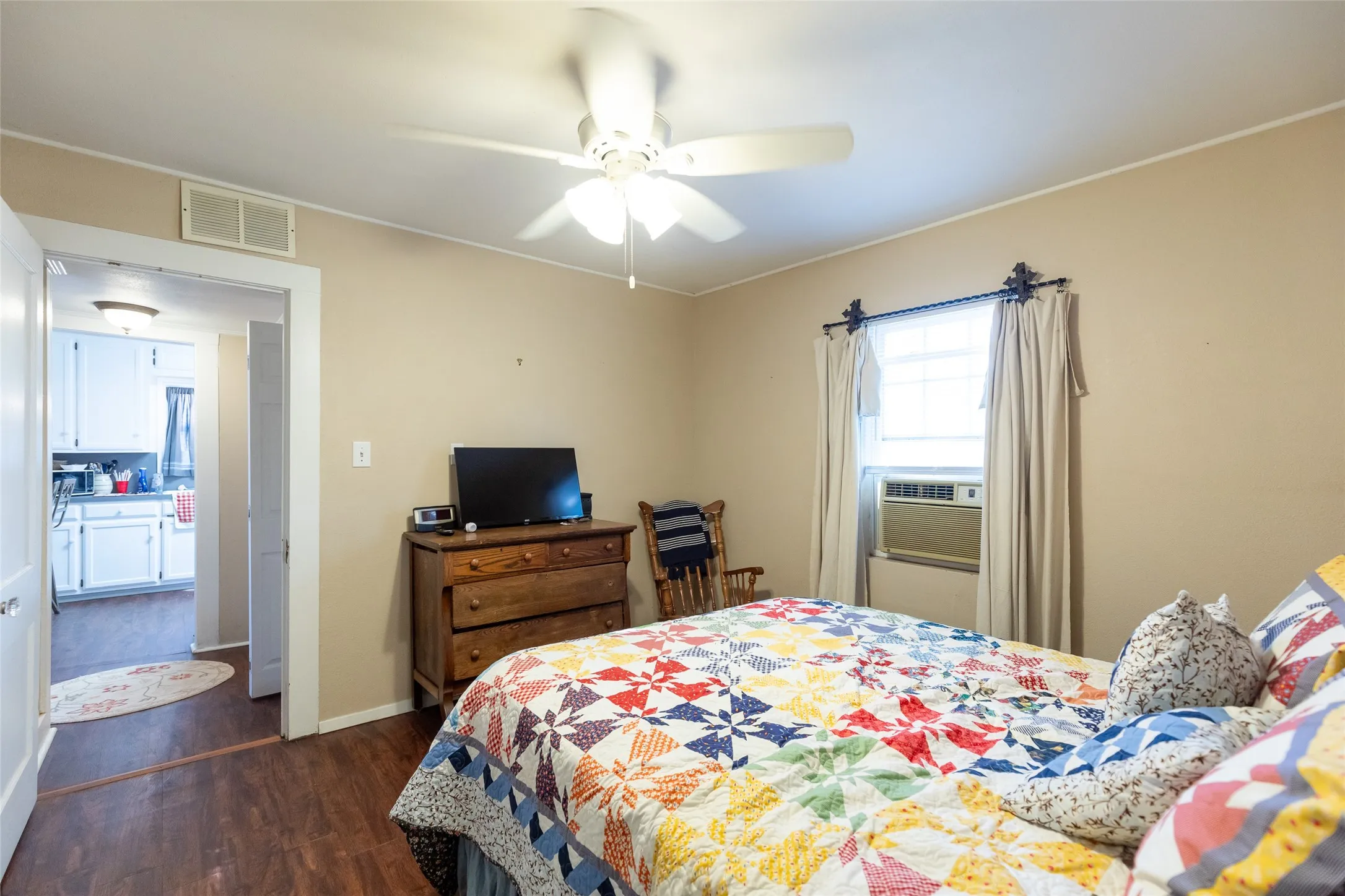 Wood-finish flooring throughout, ceiling fan with integrated lighting, and window with an in-wall air conditioning unit