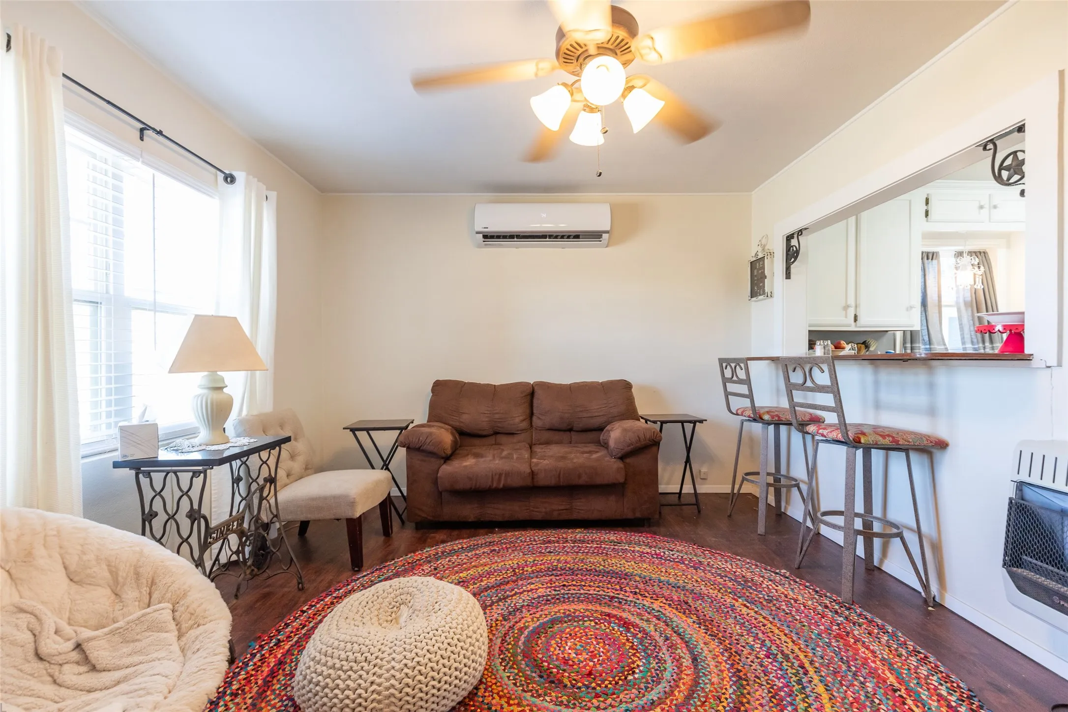 Hardwood-finish flooring, ceiling fan with integrated lighting, a split air conditioning unit, and a pass-through bar with seating