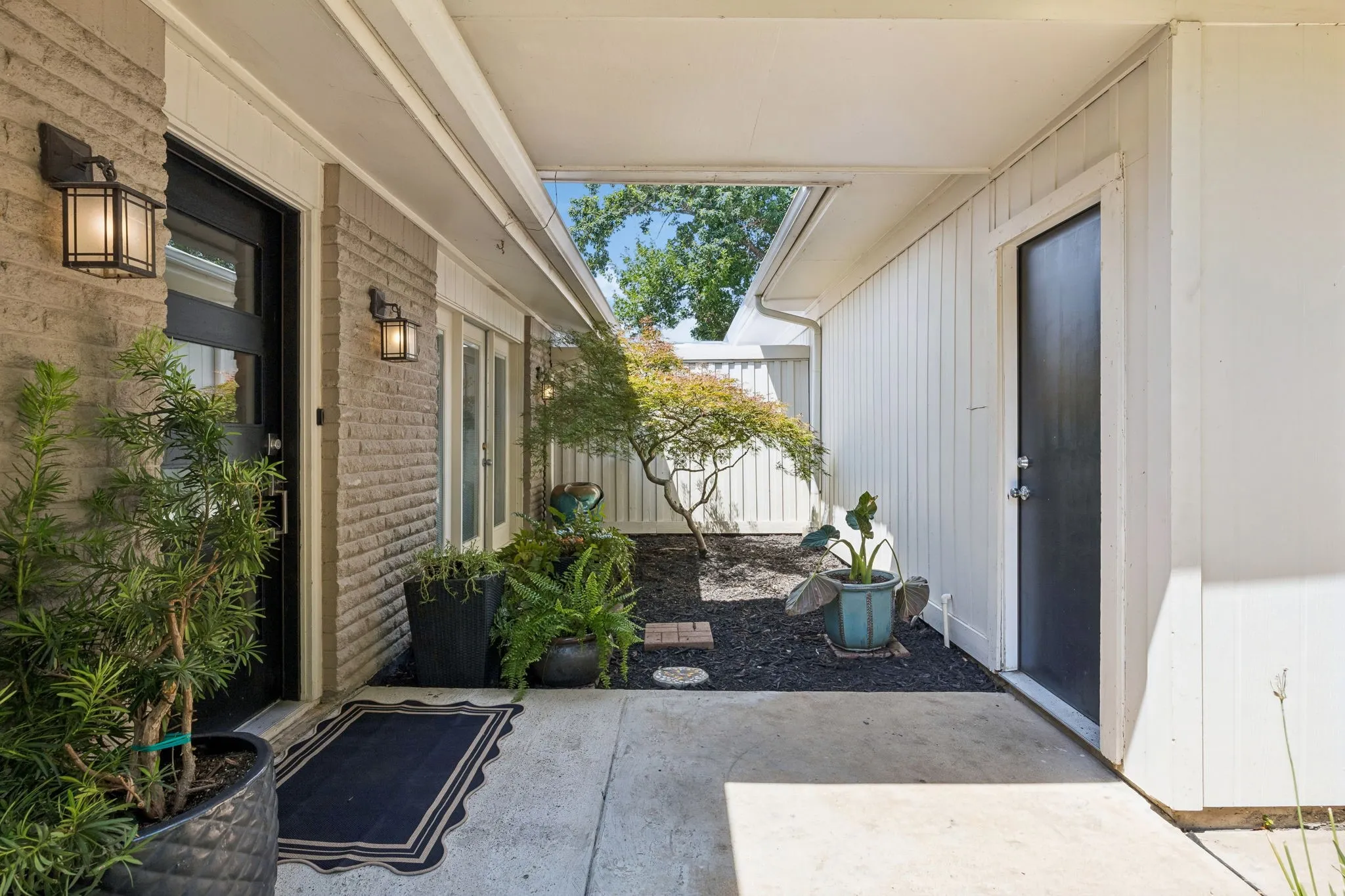 Covered entryway featuring brick facade, two exterior wall sconces, a dark paneled front door, and a  walkway