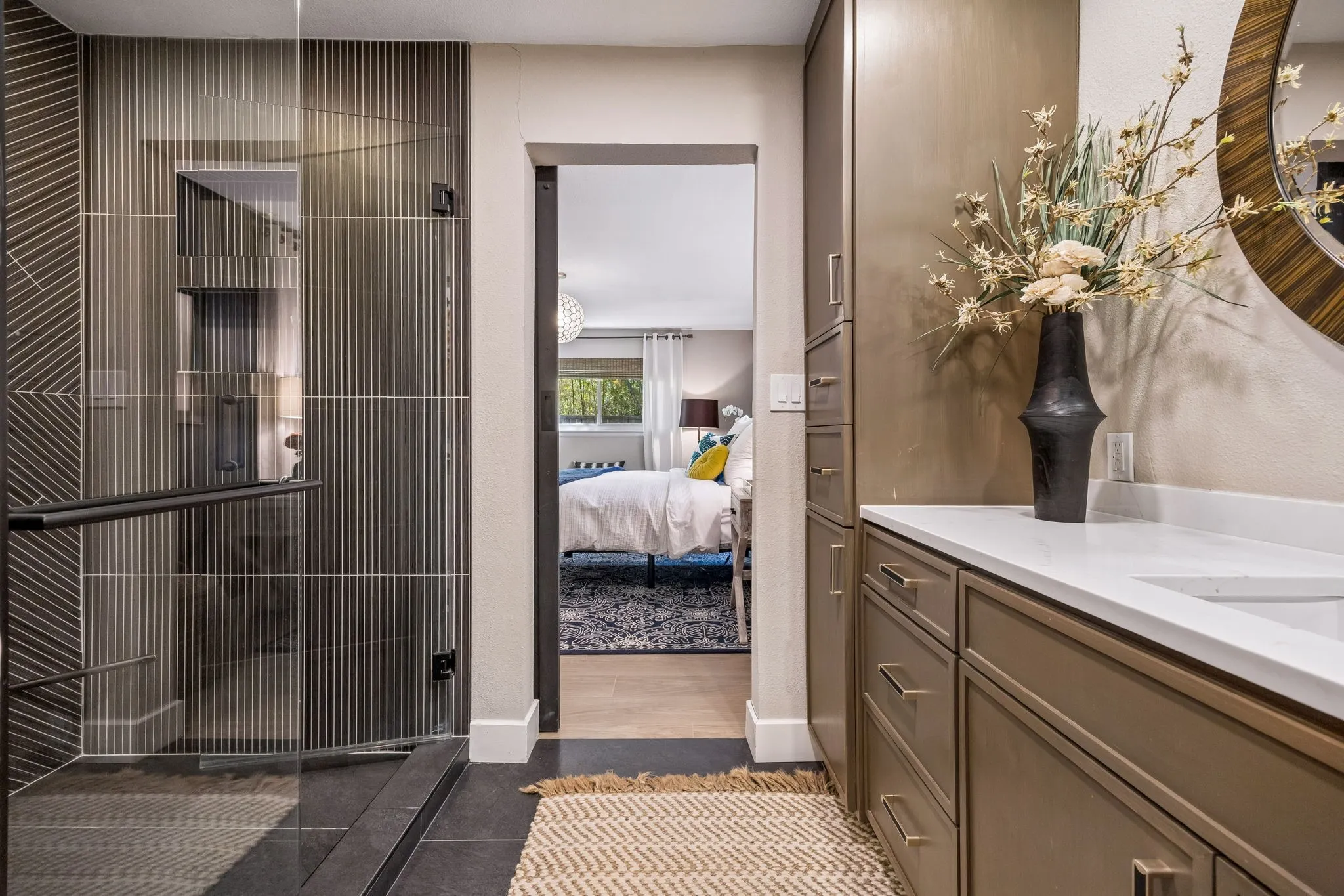 Glass-enclosed shower with ribbed tile, built-in vanity with white quartz countertop, and integrated cabinetry