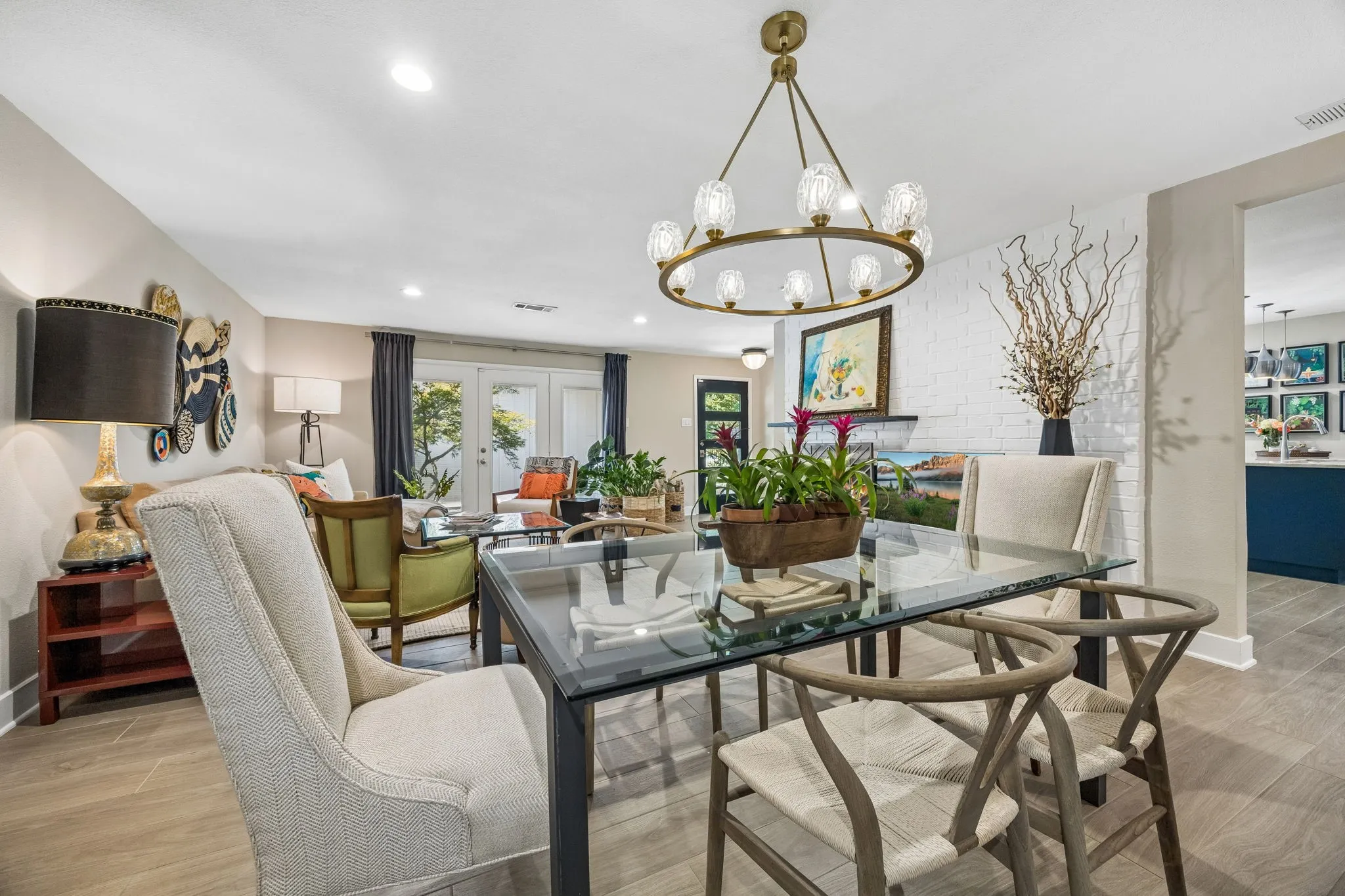 Open-concept living space tile flooring, a contemporary chandelier, white brick accent wall, and double French doors