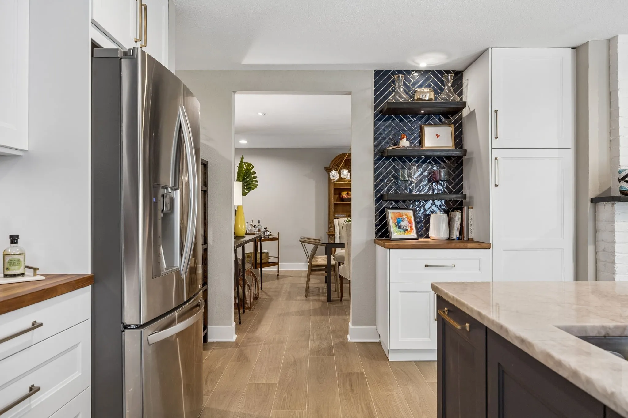 Stainless steel refrigerator, white cabinetry, dark wood-finish open shelving, herringbone tile backsplash, and light wood-finish flooring