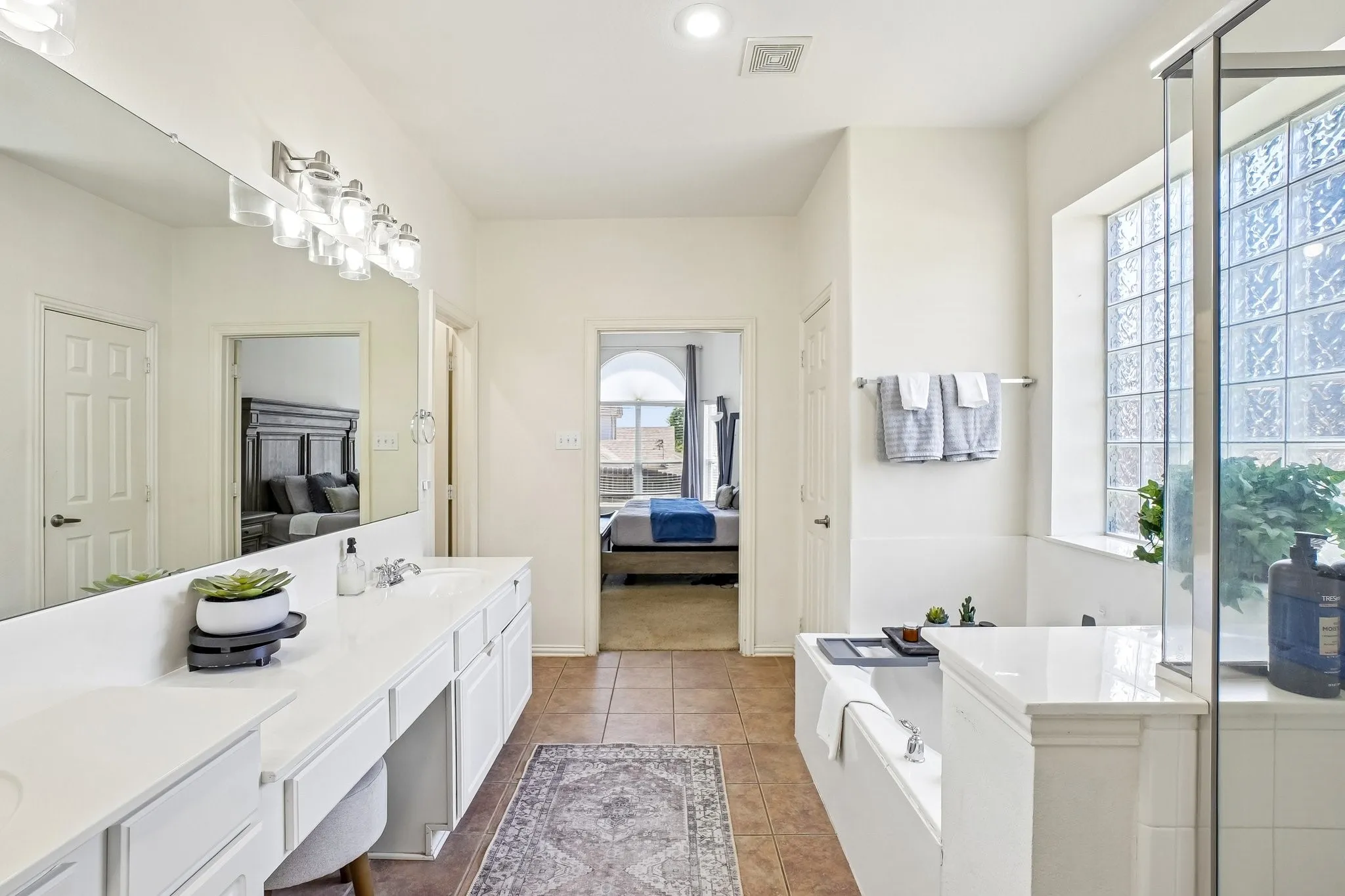 Bathroom featuring a double vanity with ample counter space, a built-in soaking tub, and a separate glass-enclosed shower with a glass block window