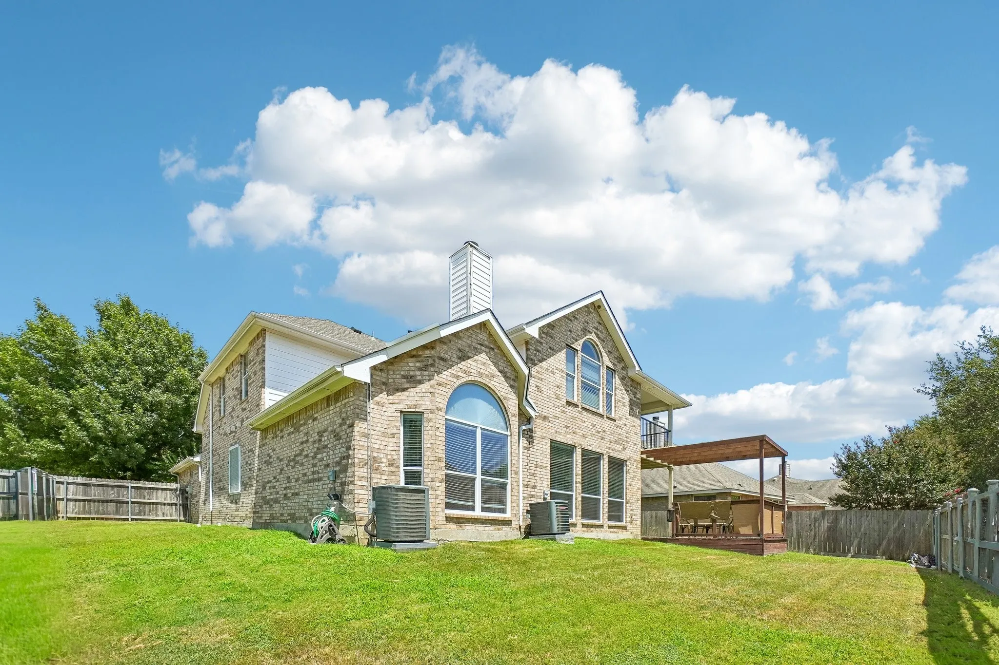 Spacious backyard featuring a brick exterior, arched window, wood deck, and a pergola