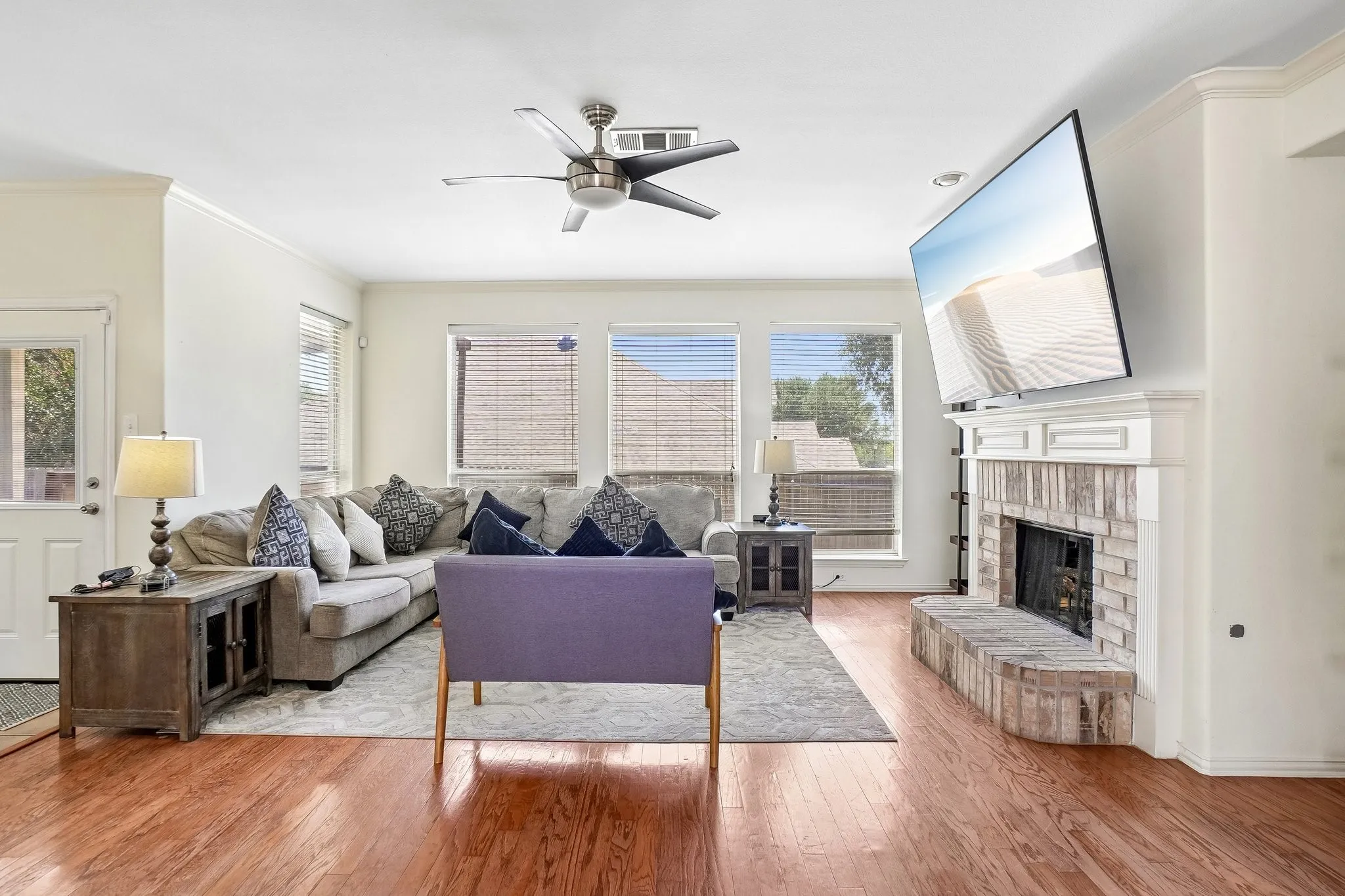 Hardwood-finish flooring throughout, featuring a fireplace with brick surround and hearth, white mantel, and ceiling fan