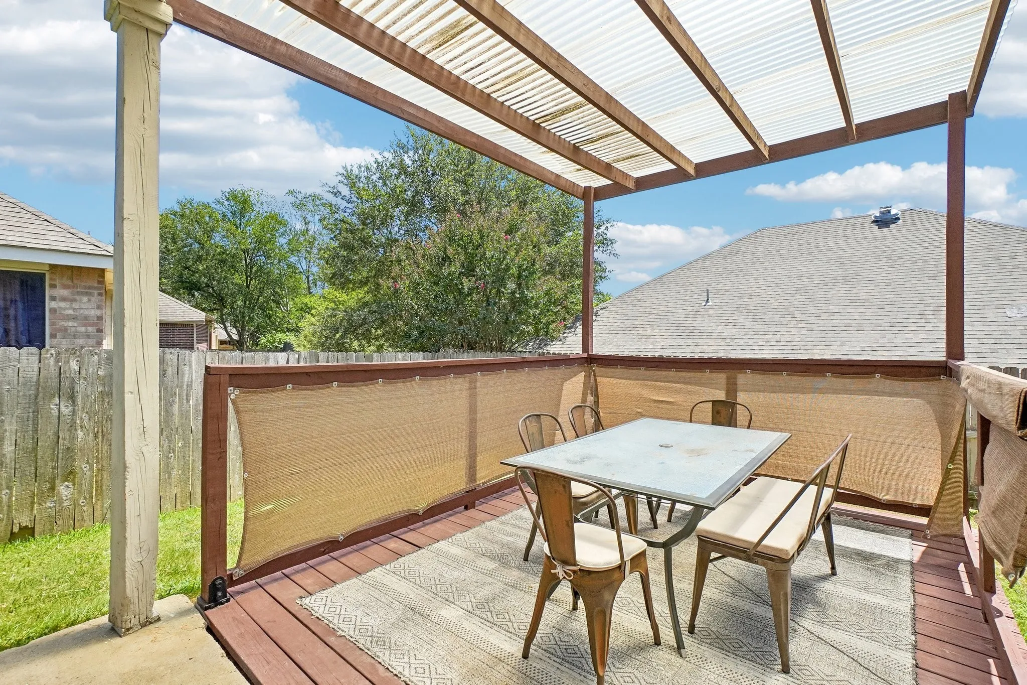 Elevated wooden deck featuring a translucent corrugated roof, a privacy screen, and a textured area rug