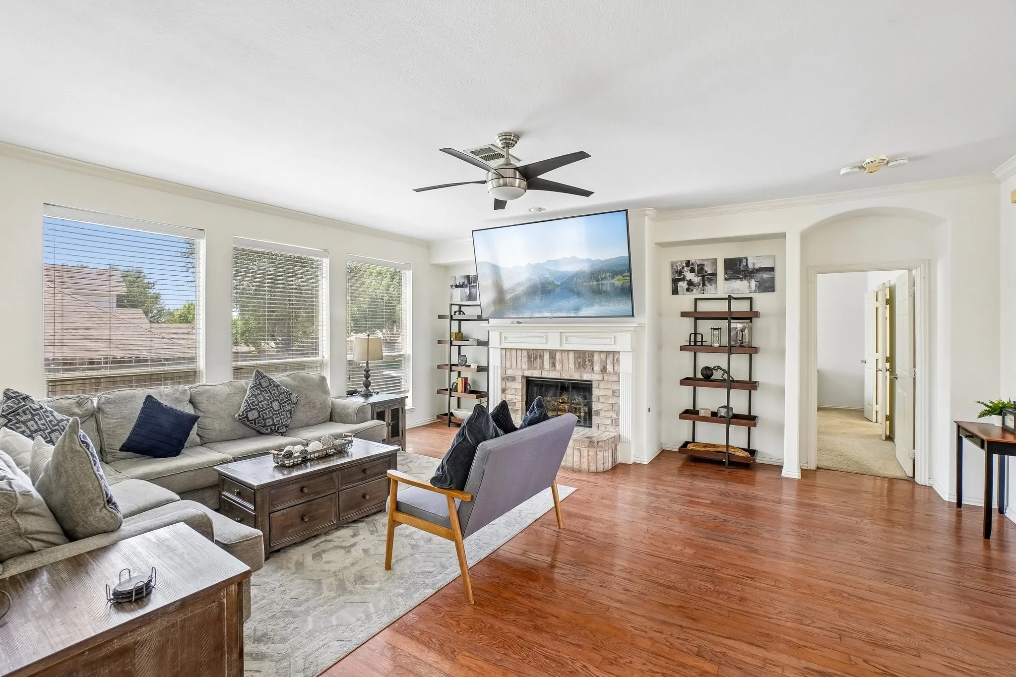 Spacious living area featuring rich wood-finish flooring, a brick fireplace with a white mantle, an arched doorway, and built-in shelving
