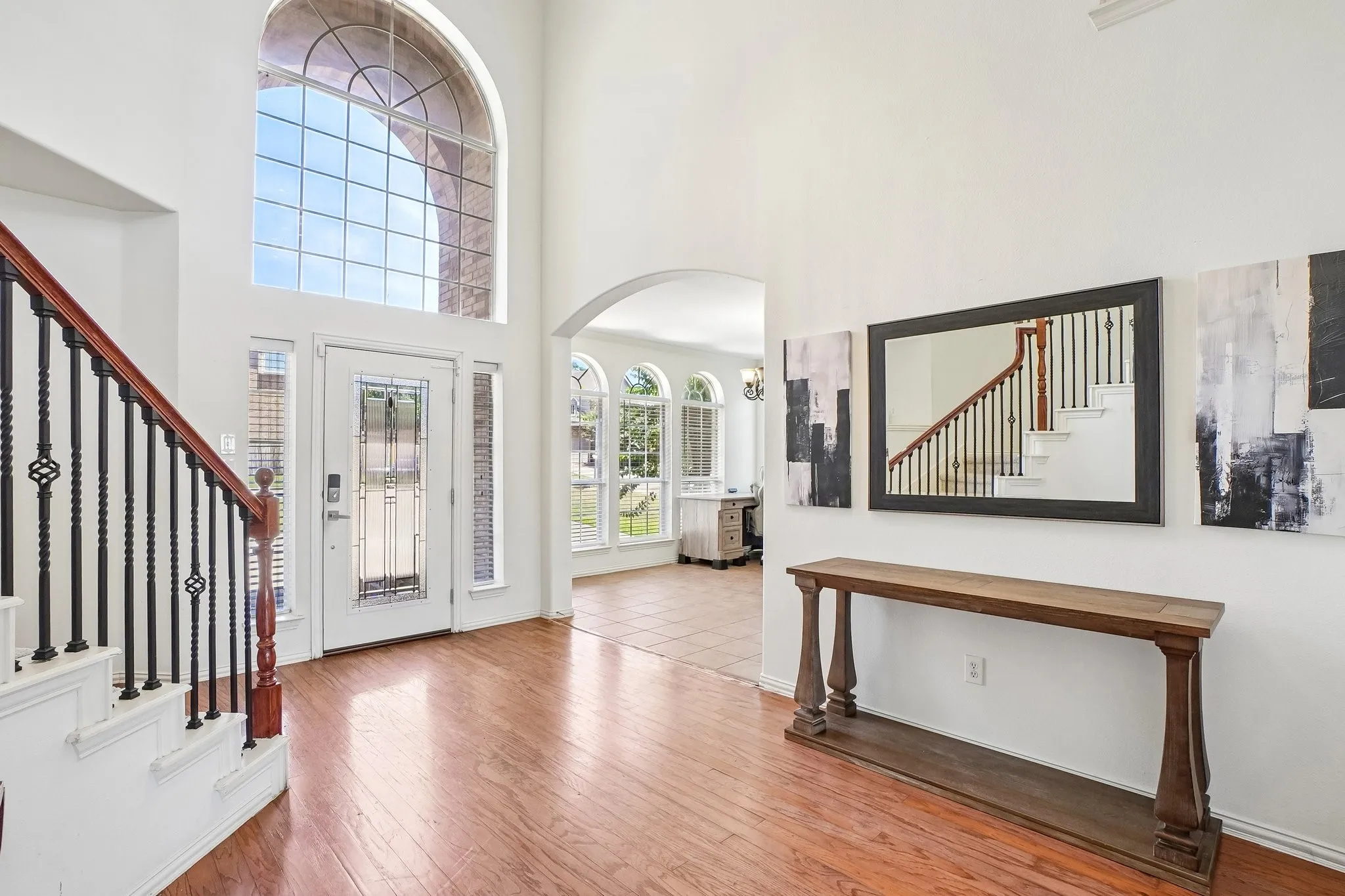 Two-story foyer featuring wood-finish flooring, a grand arched window, a staircase with wood newel posts and railings, decorative metal balusters, and an arched entryway