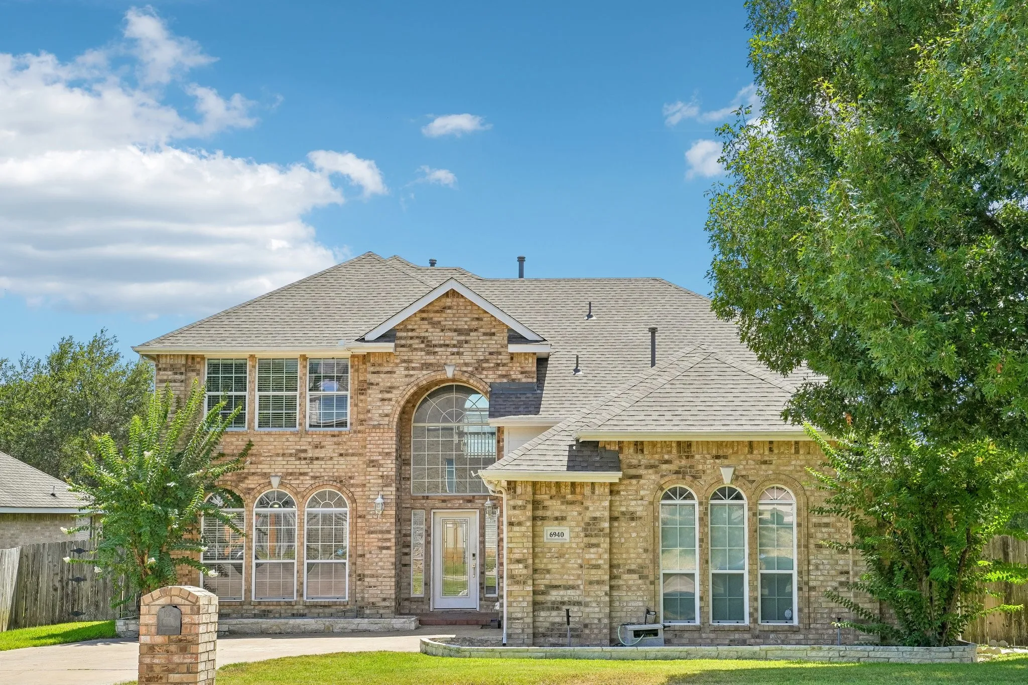 Brick facade residence featuring a prominent arched window entry, multiple arched windows, a multi-gabled roofline, and an attached brick mailbox