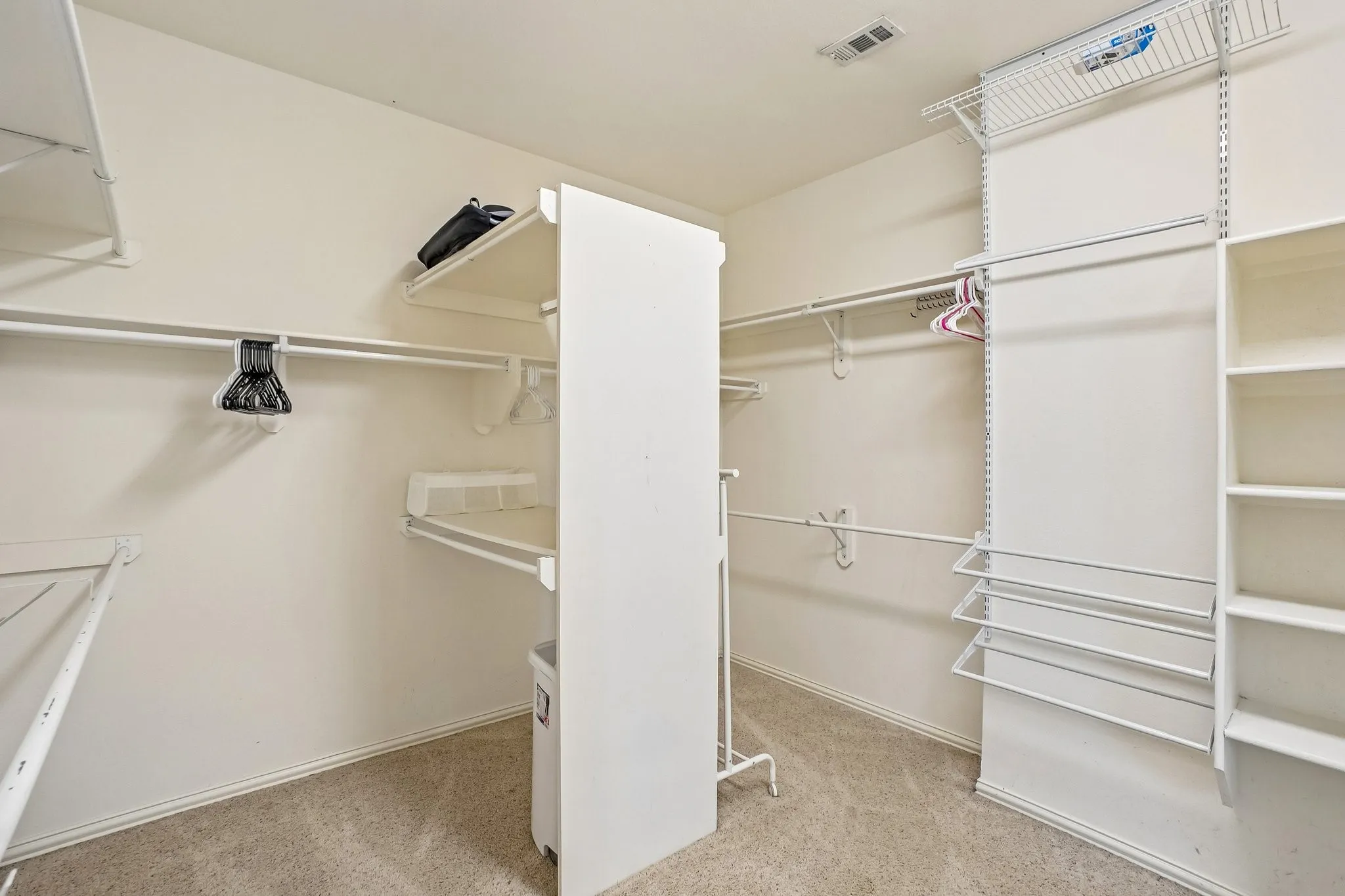 Walk-in closet featuring extensive white shelving, multiple hanging rods, built-in shoe racks, and light-toned carpet flooring