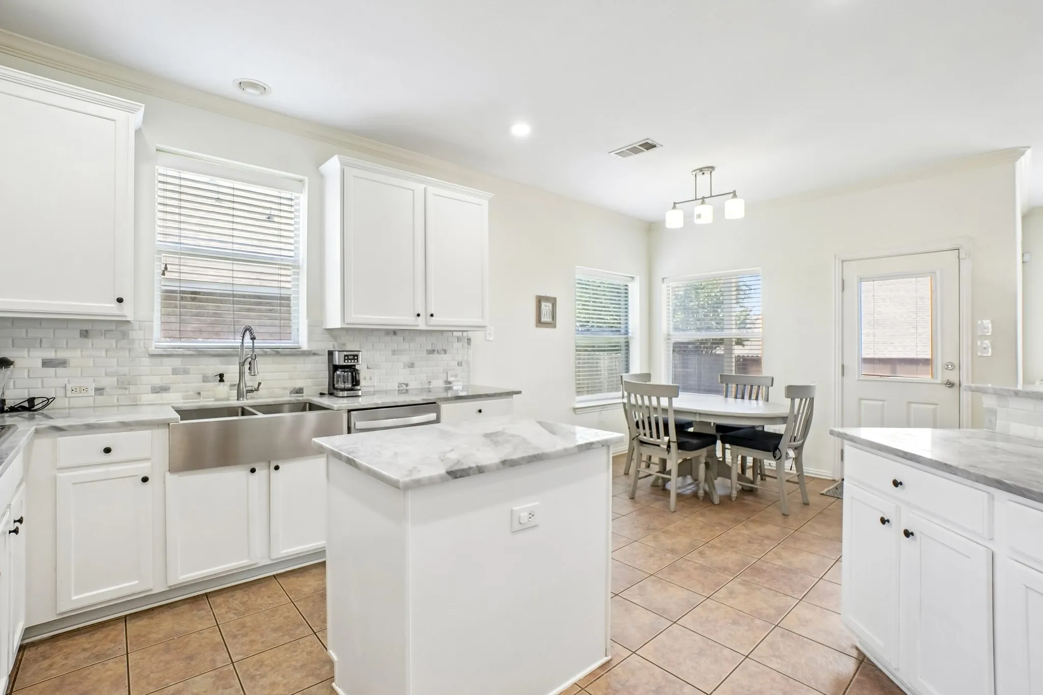 Kitchen featuring white cabinetry, stainless steel farmhouse sink, mosaic tile backsplash, and light-toned countertops