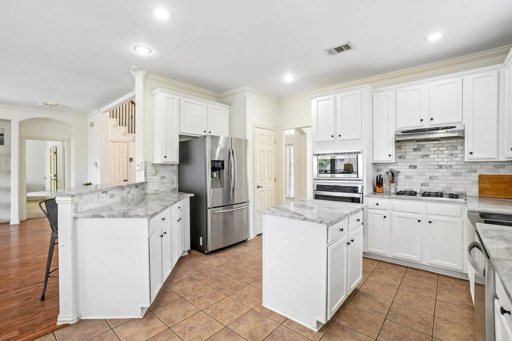 Modern kitchen featuring white cabinetry, stainless steel appliances, a center island, and natural stone countertops with a complementary subway tile backsplash