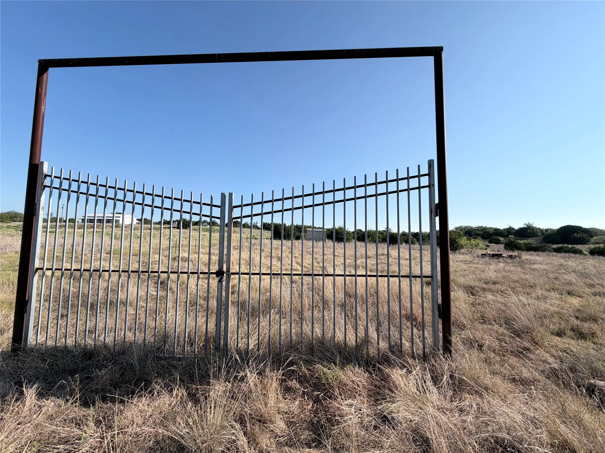 Wrought iron gate with a metal frame entrance, set within an expansive, undeveloped property