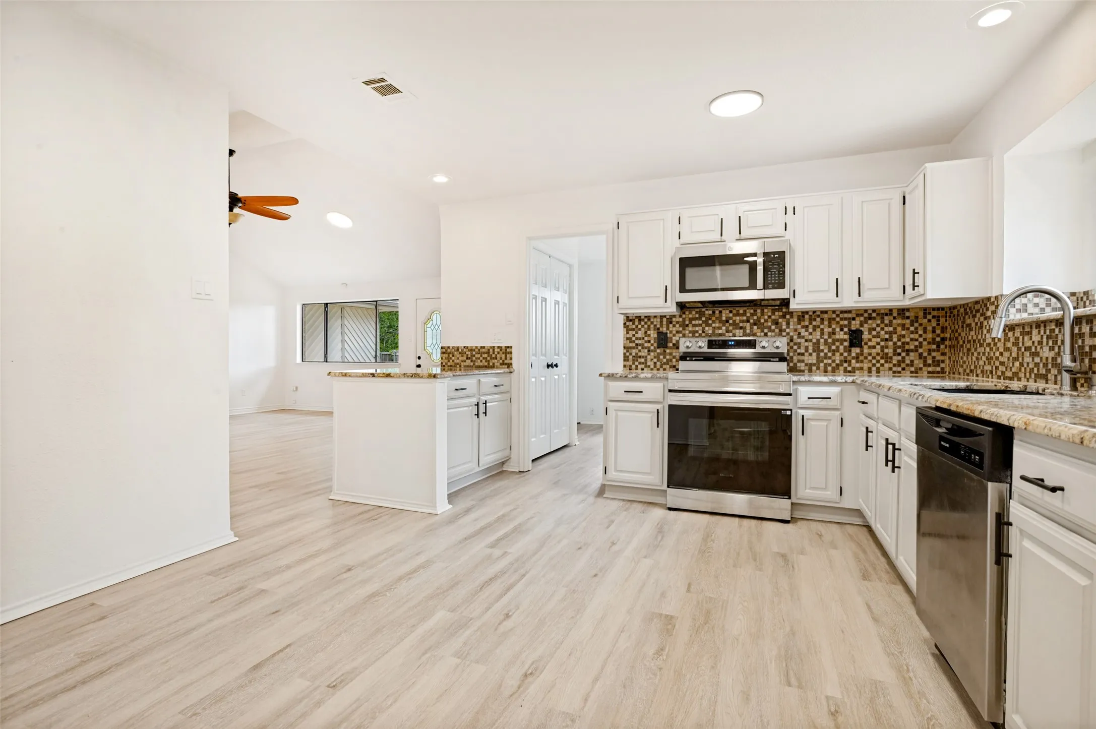 Kitchen featuring stainless steel appliances, white cabinetry, granite countertops, and mosaic tile backsplash
