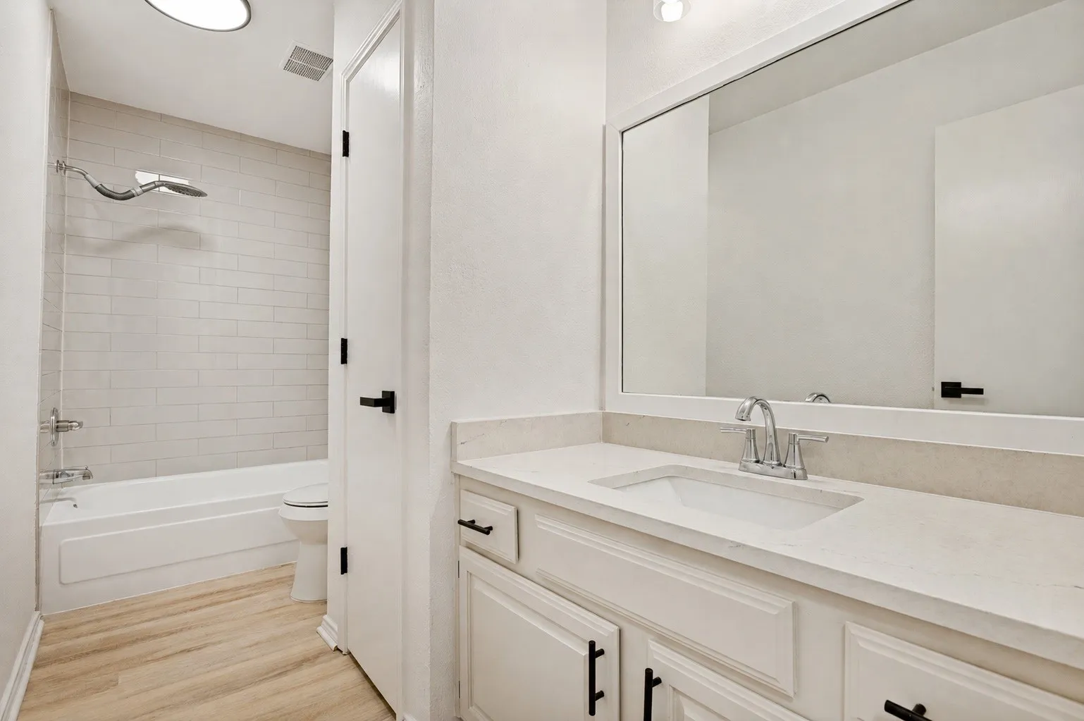 White subway tile shower surround, single vanity with light-toned countertop, undermount sink, and wood-finish flooring