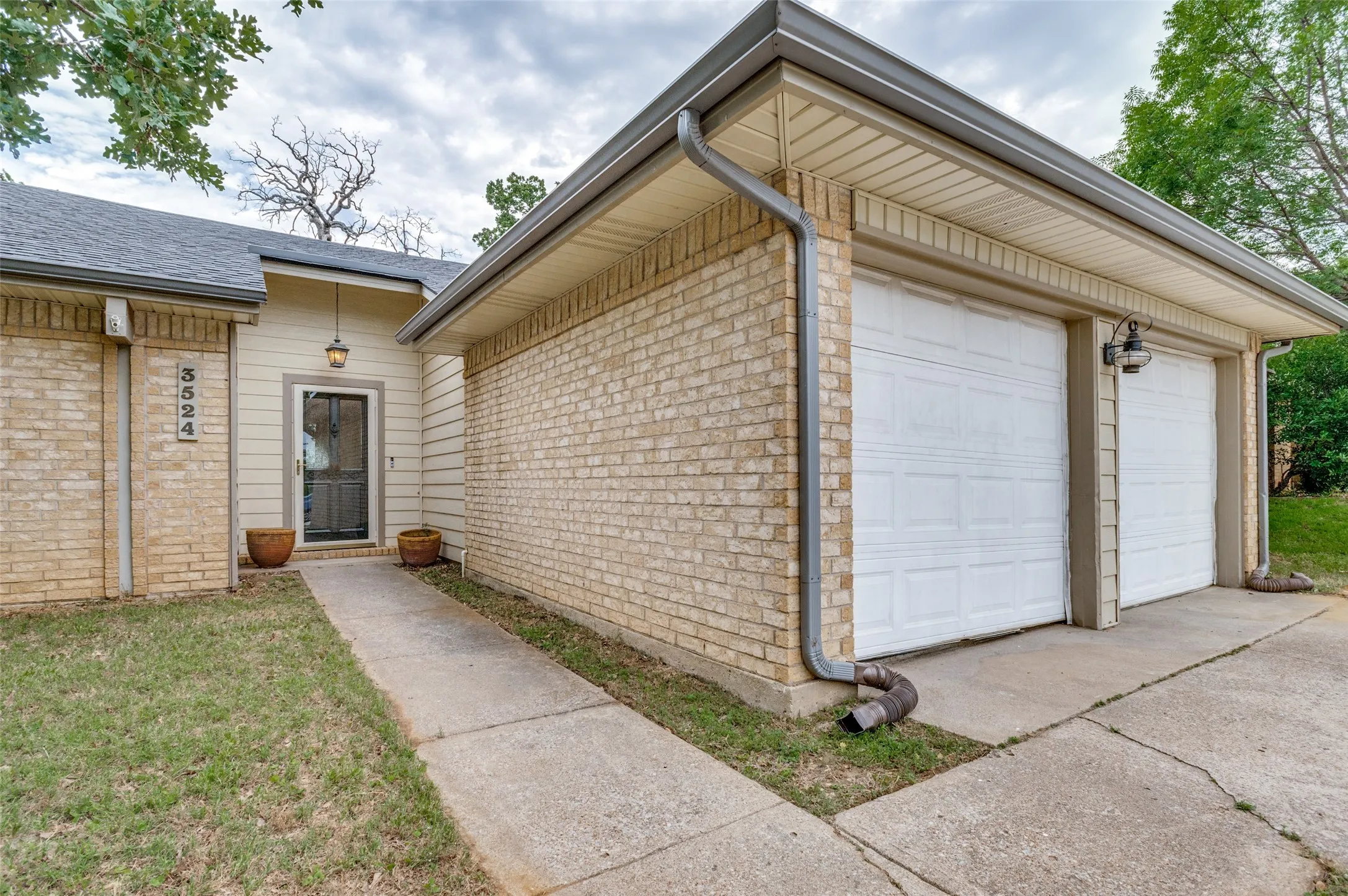 Brick facade with siding accents, two-car garage, concrete driveway, front entry with an overhead light fixture, and a concrete walkway