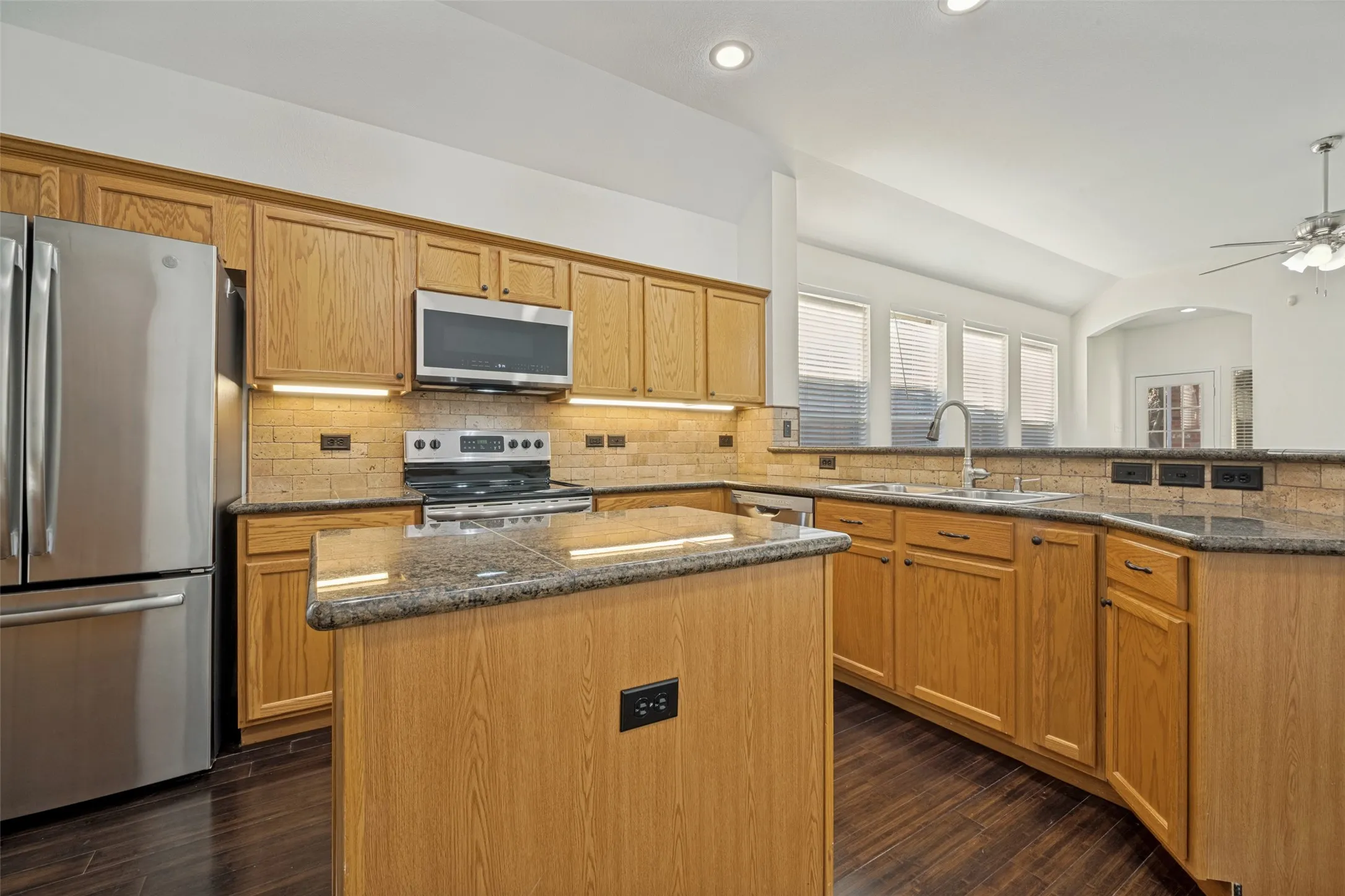 Kitchen featuring wood-finish cabinetry, stainless steel appliances, granite countertops, tile backsplash, and recessed lighting