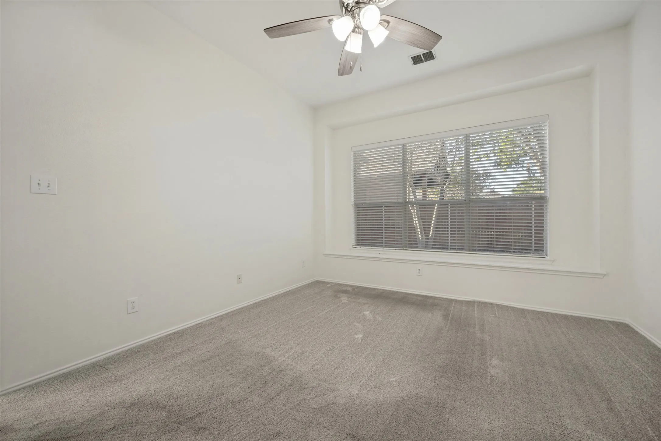 Vaulted ceiling with a ceiling fan, large window with blinds, and light-toned carpet flooring
