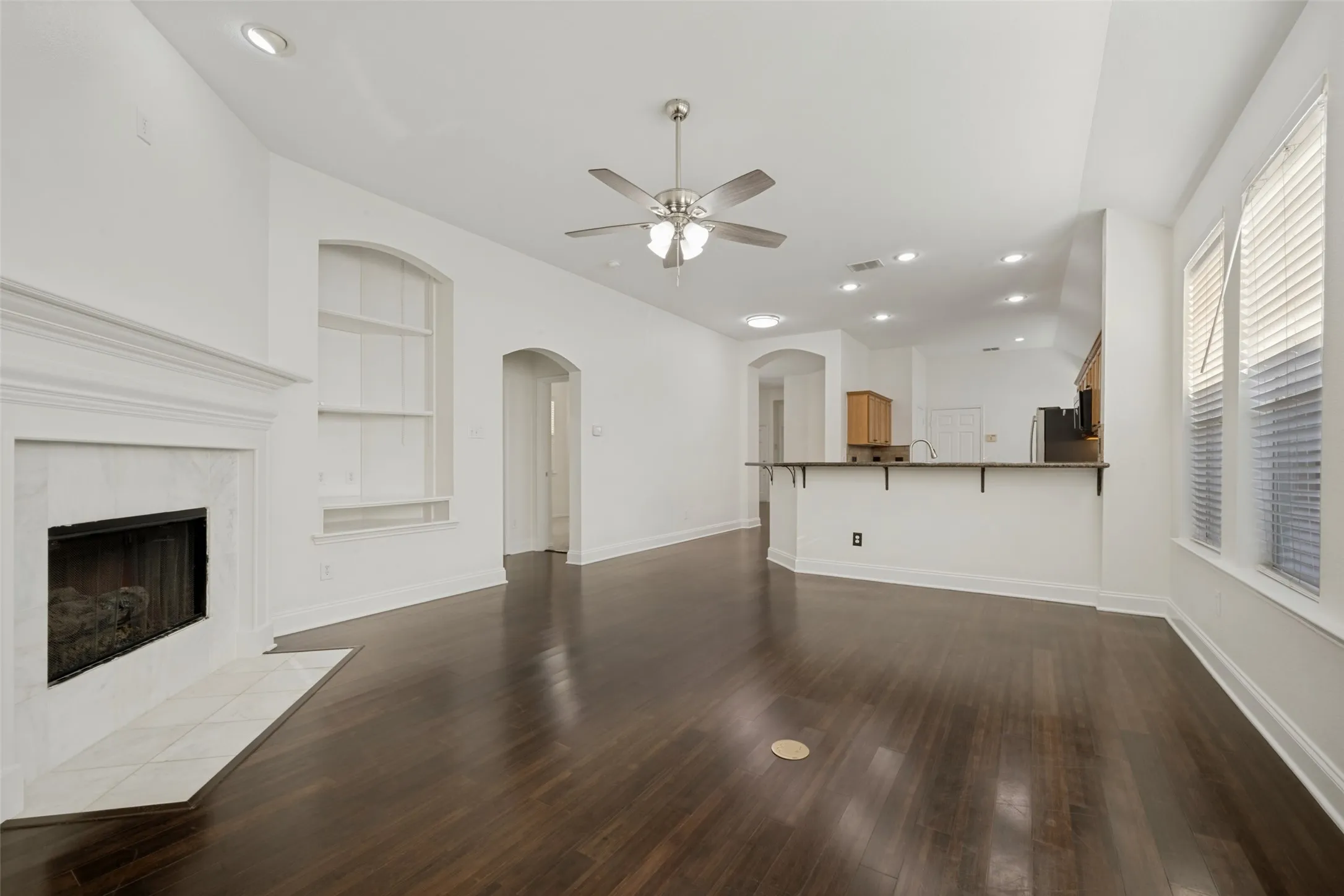 Vaulted ceiling with recessed lighting, dark wood-finish flooring, built-in shelving, stone-tiled fireplace, and a breakfast bar with stone countertop
