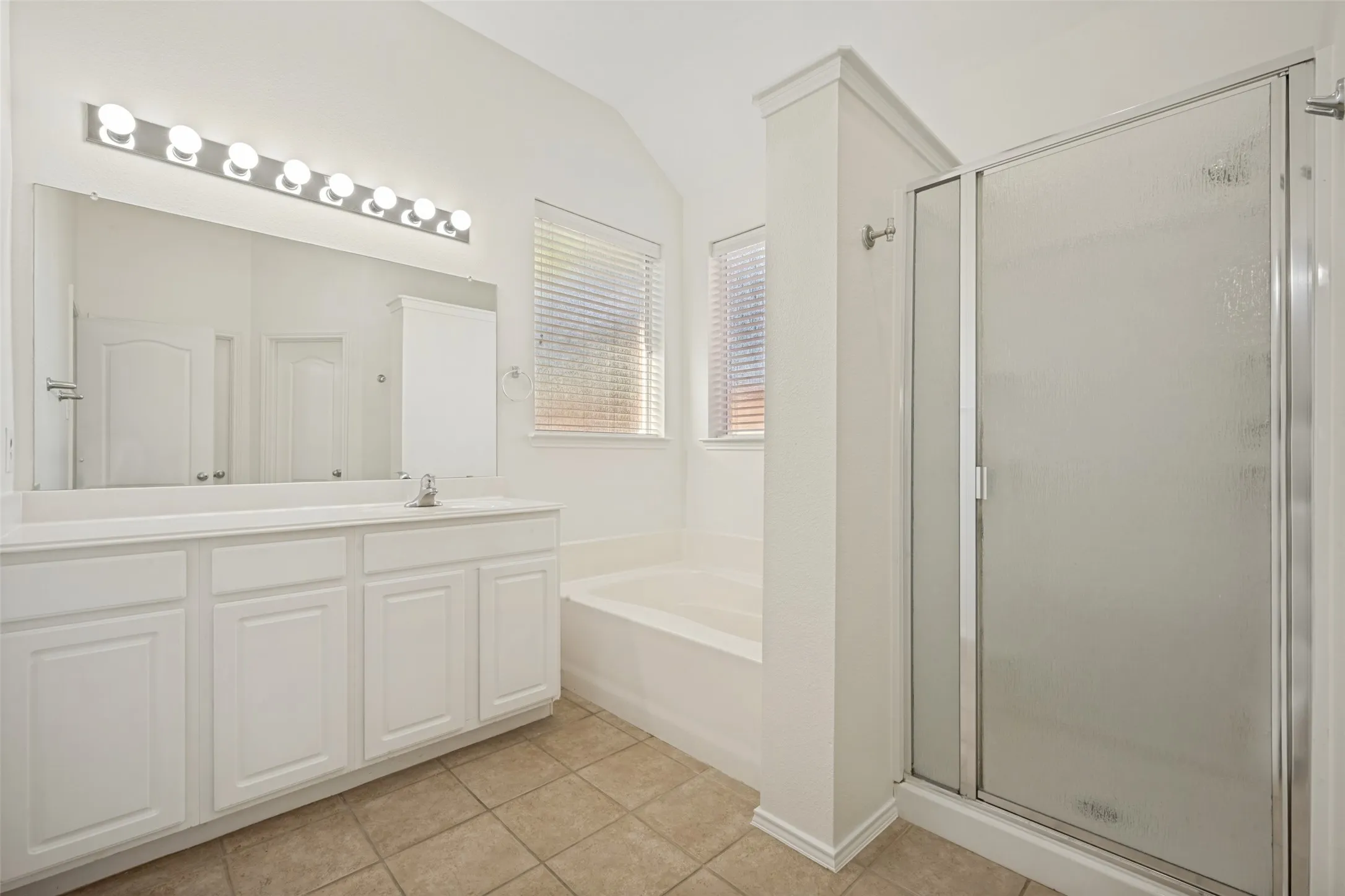 White vanity with extensive storage, full-width mirror, tile flooring, built-in tub, and glass-enclosed shower