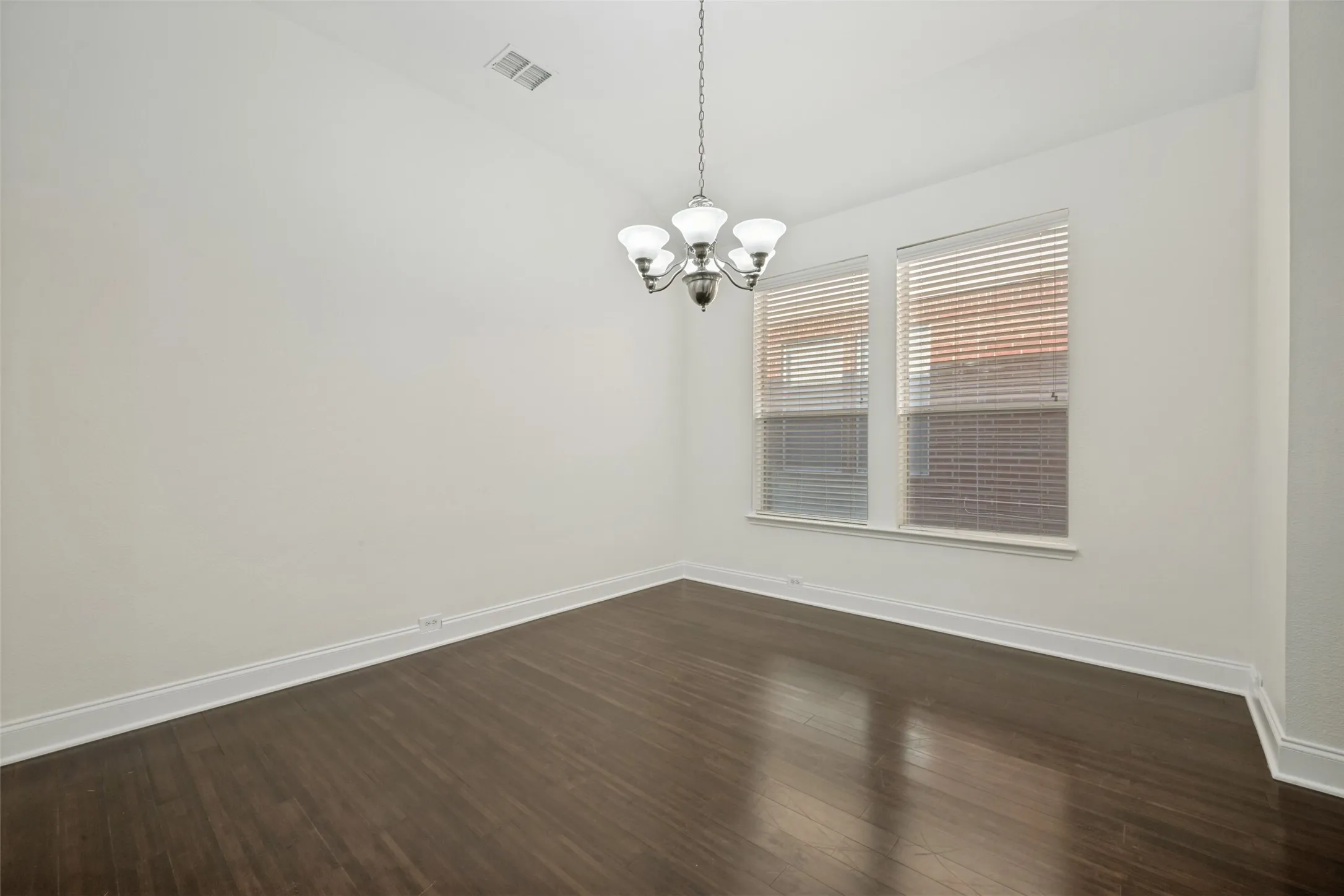 Dark wood-finish flooring, white baseboards, a suspended chandelier, and two windows with blinds