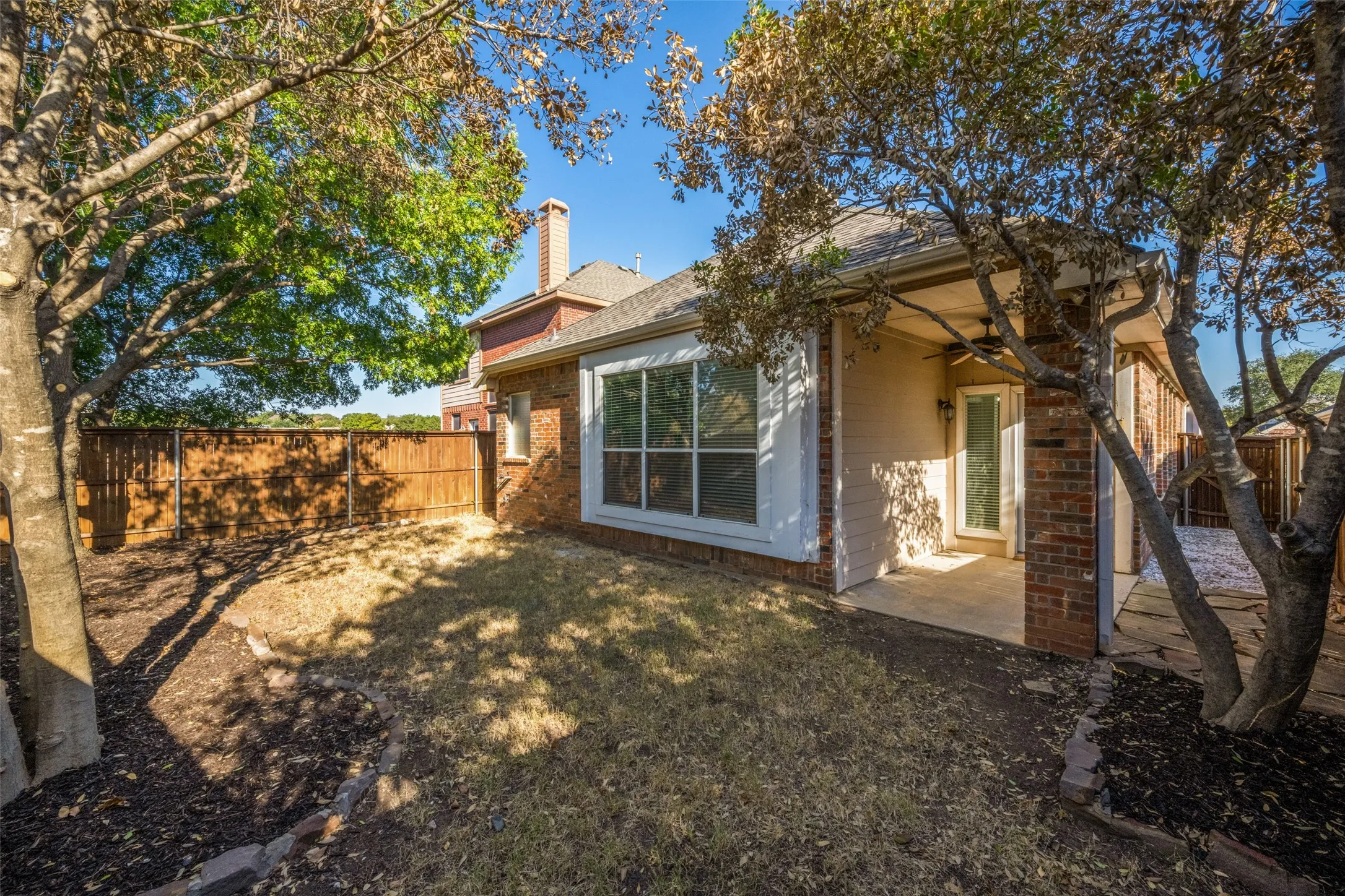 Private backyard with brick and stucco exterior, a wood fence, and mature trees