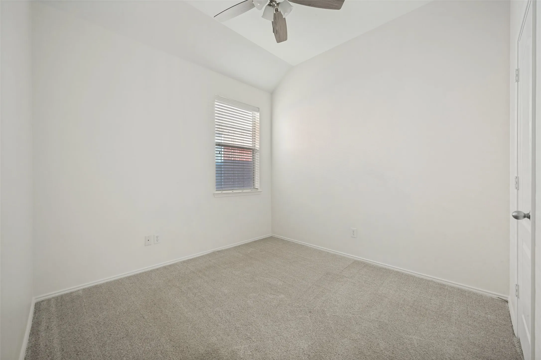 Neutral-toned carpet flooring, light-colored walls, window with blinds, and a ceiling fan