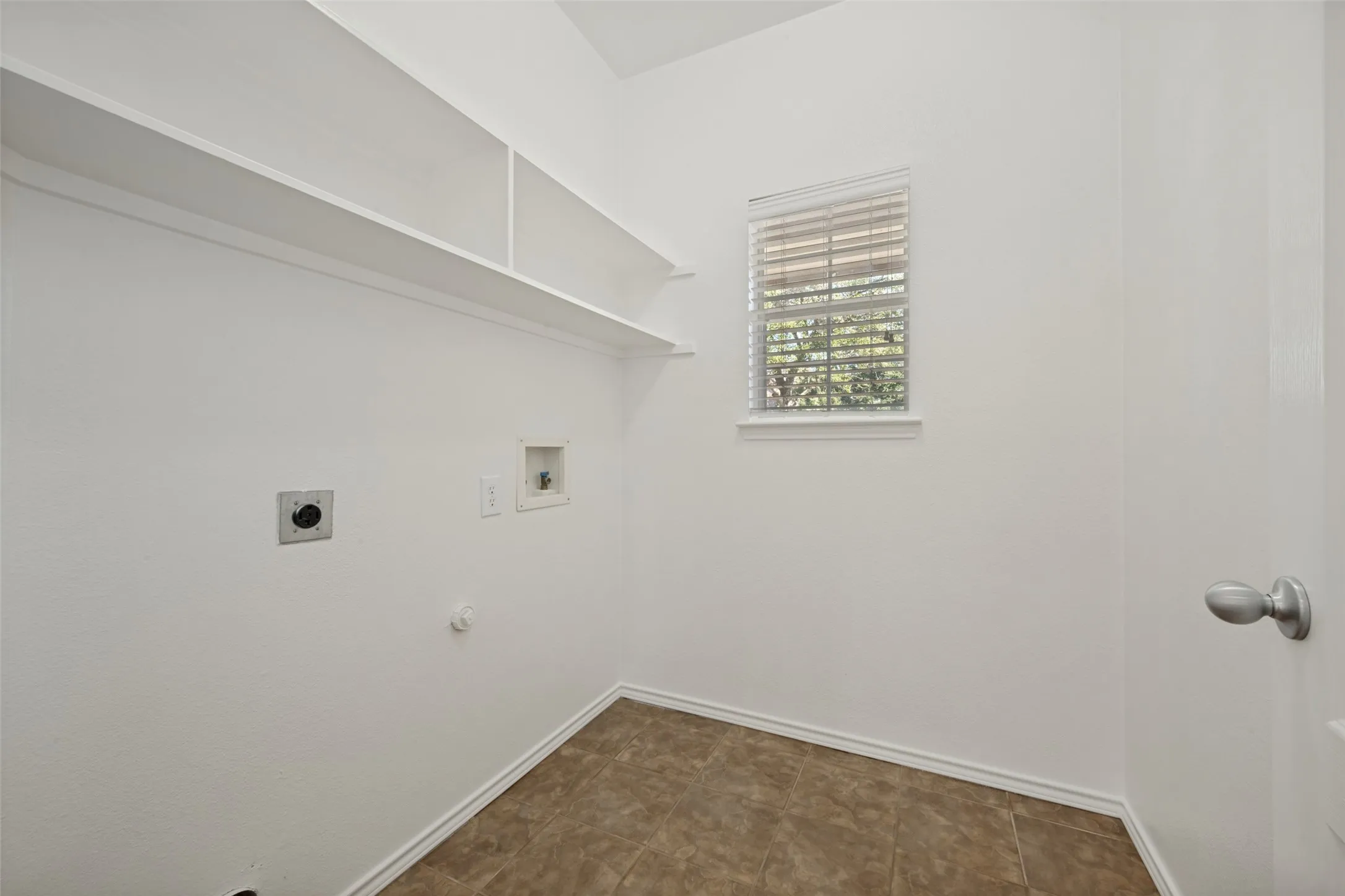 Spacious utility room featuring built-in shelving, a single window with blinds, and tile flooring