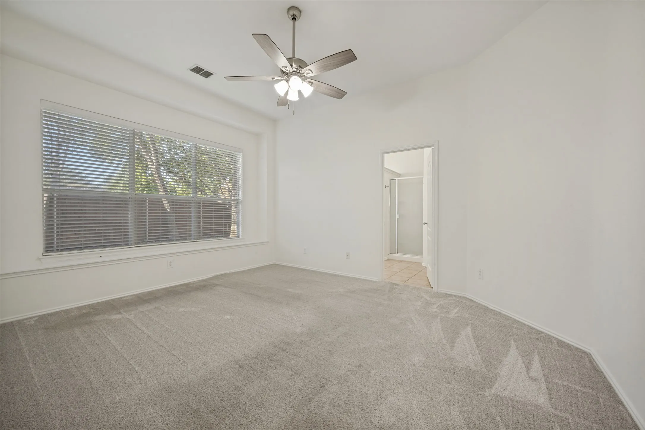 Spacious room with plush carpet, a large window with blinds, and a ceiling fan with integrated lighting