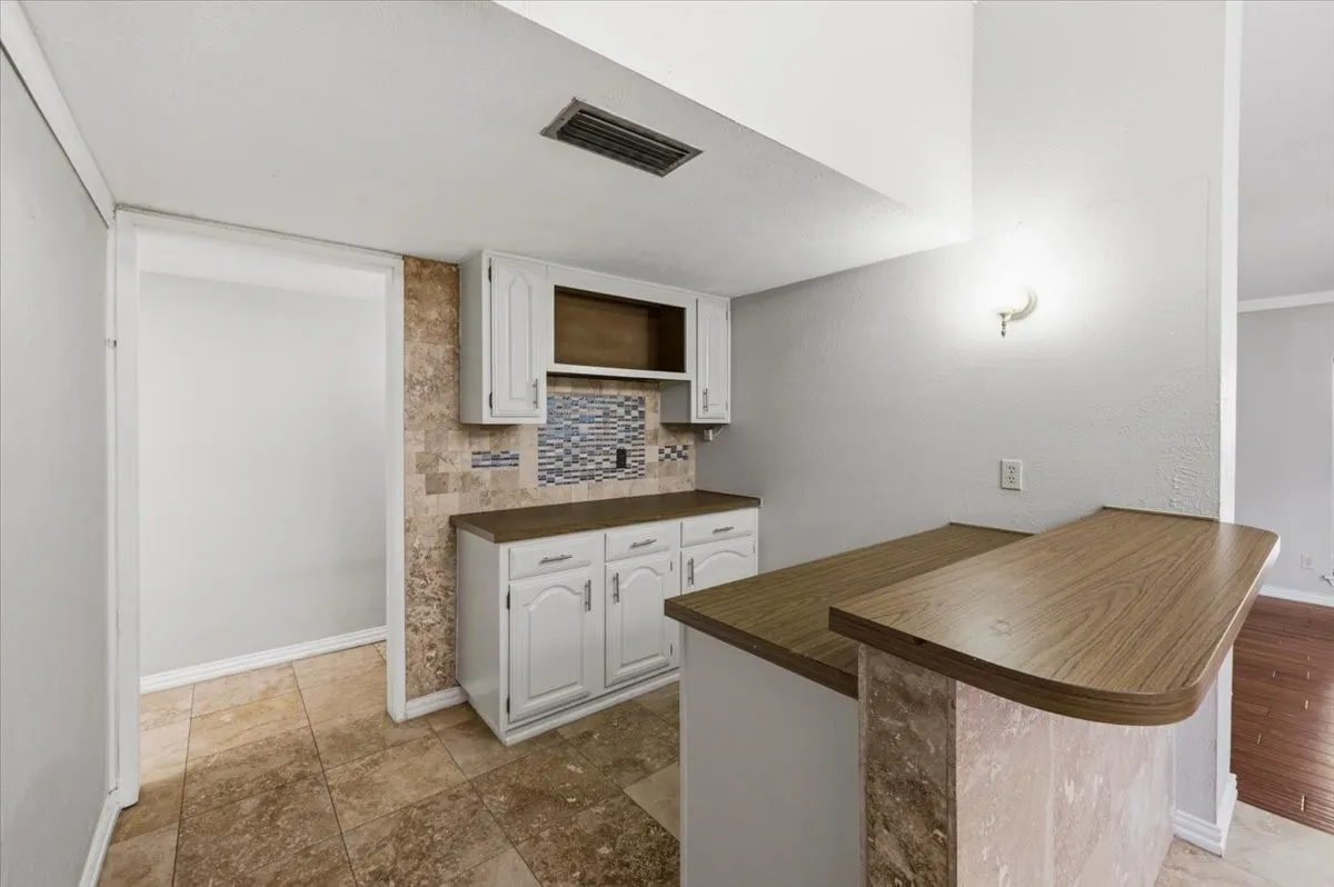 Dining Area features a closer view of the built-in butlers pantry cabinetry with tile backsplash, with a hallway beyond leading toward the breakfast nook and kitchen. Tile flooring extends throughout.
