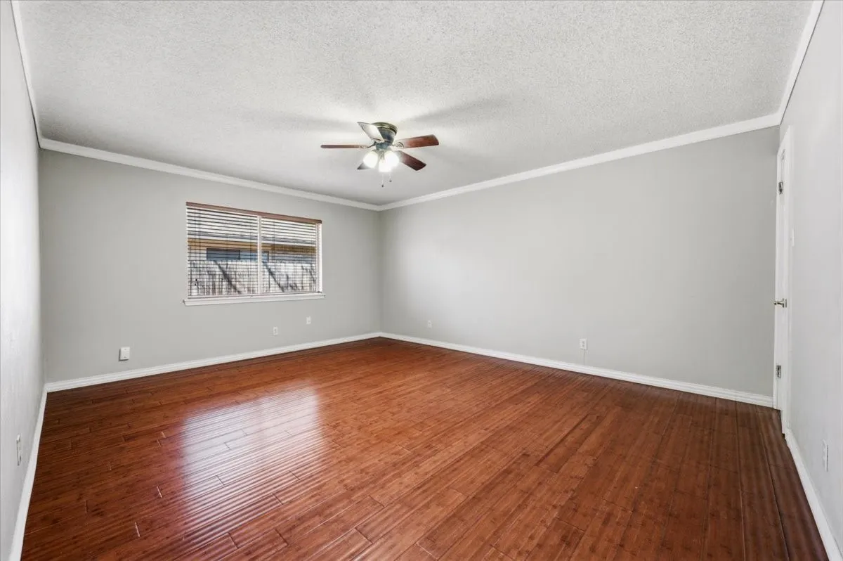 Primary Bedroom features crown molding and ceiling fan with light fixture, with a single window bringing in natural light. Wood flooring extends throughout.