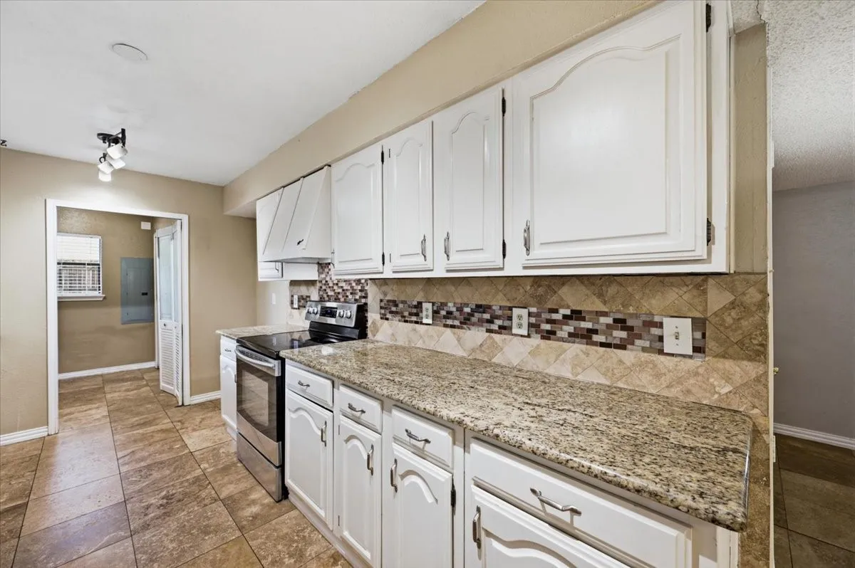 Kitchen features a closer view of the granite countertops and tile backsplash along the cabinetry, with a doorway opening to the utility room. Tile flooring extends throughout.
