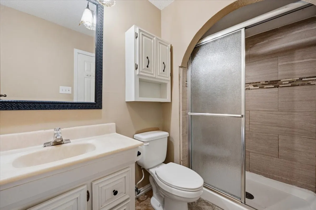 Primary Bathroom features a walk-in shower with an arched entry and tile surround, alongside a single vanity and built-in cabinet storage above the toilet. Tile flooring extends throughout.