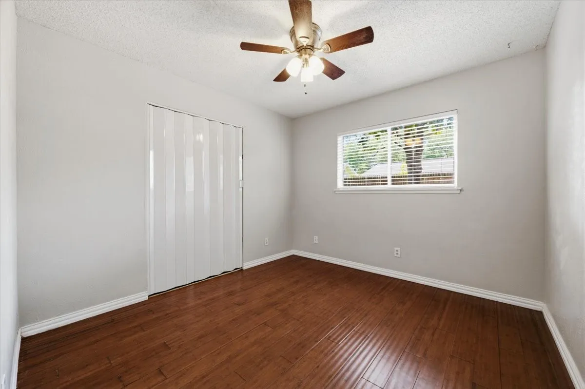 Secondary Bedroom features ceiling fan with light fixture, a bifold closet door, and a single window. Wood flooring extends throughout.