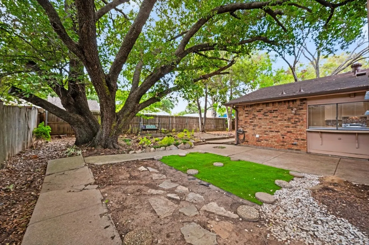 Backyard features a wide concrete walkway extending along the rear of the home, framed by mature trees and wood privacy fencing.