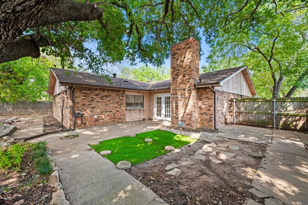 Rear Exterior features a brick chimney and French doors opening to the backyard. Wood fencing encloses the yard, which is shaded by mature trees.