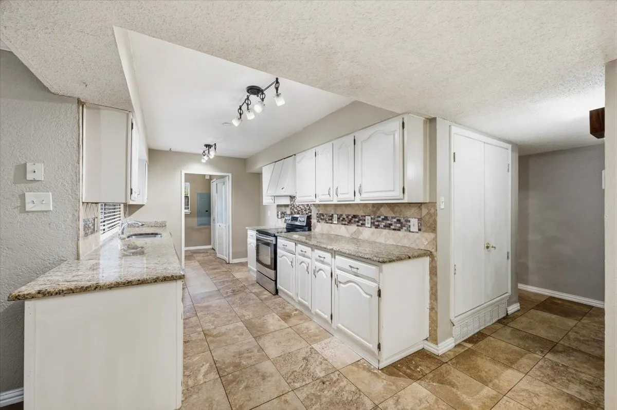 Kitchen features white cabinetry along the galley layout, with an AC closet and doorway leading to the hallway toward the bedrooms. Tile flooring extends throughout.