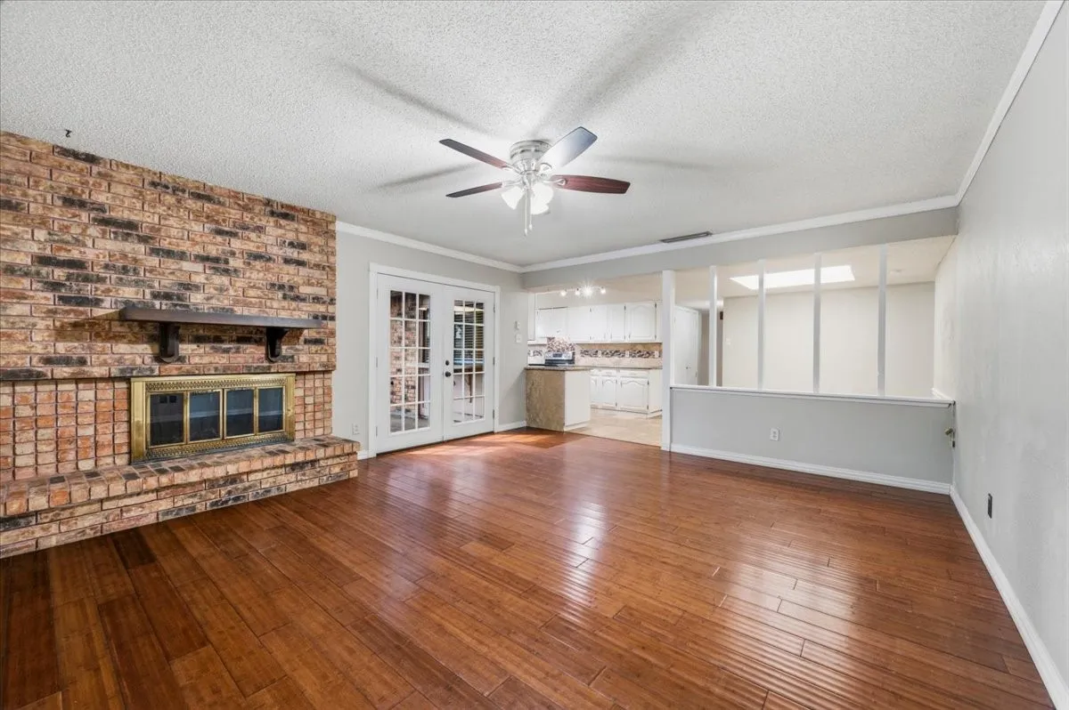 Family Room features a brick fireplace with wood mantle as the focal point, with French doors nearby leading outside. The space opens to the kitchen. Wood flooring extends throughout.