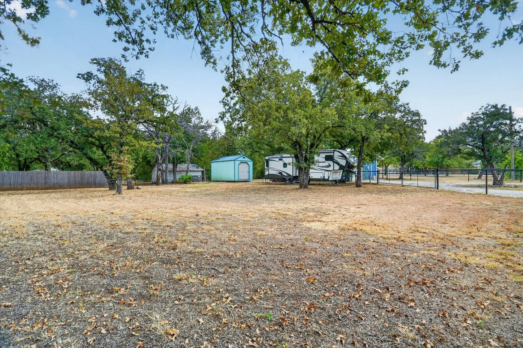 Expansive outdoor space featuring mature trees, a wooden fence, a metal shed, and a chain-link fence
