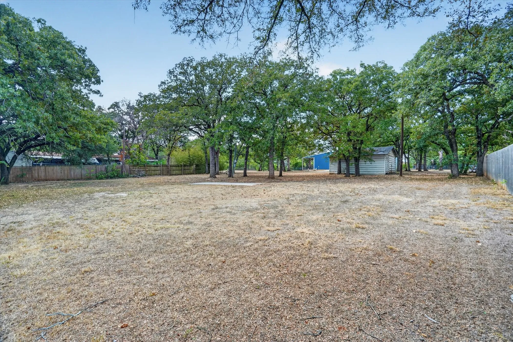 Expansive lot featuring mature trees, a wooden fence perimeter, and two detached storage structures