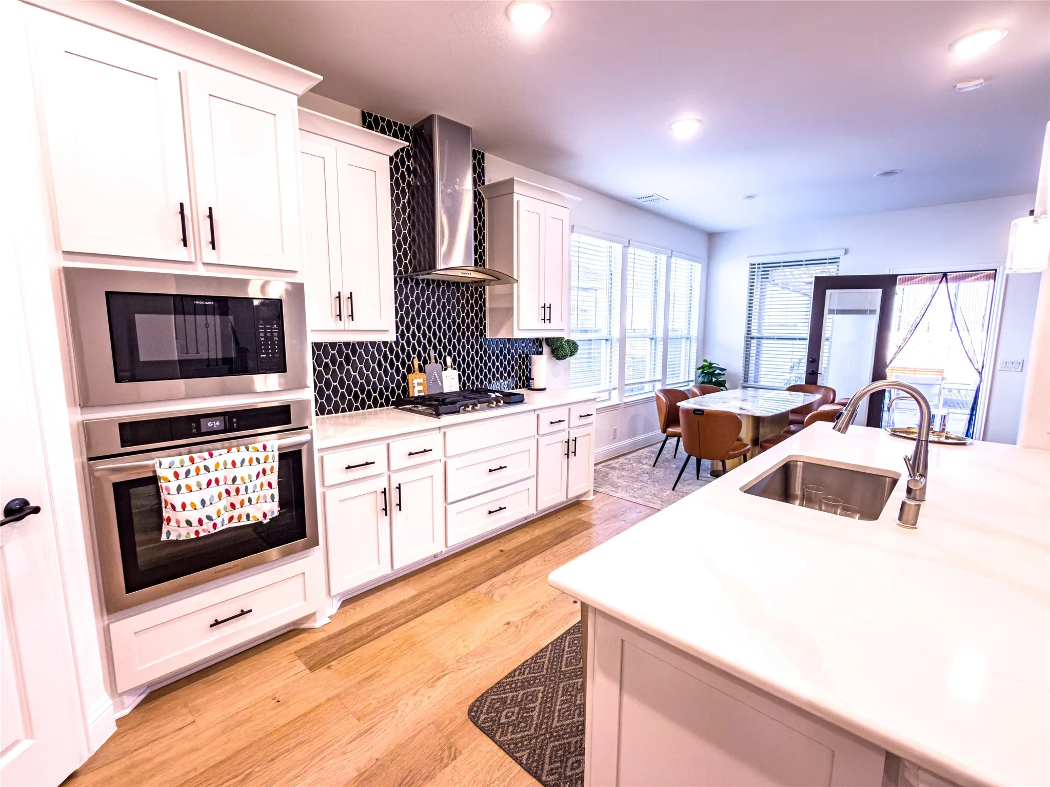 Kitchen with stainless steel appliances, light wood-type flooring, white cabinets, decorative backsplash, and recessed lighting
