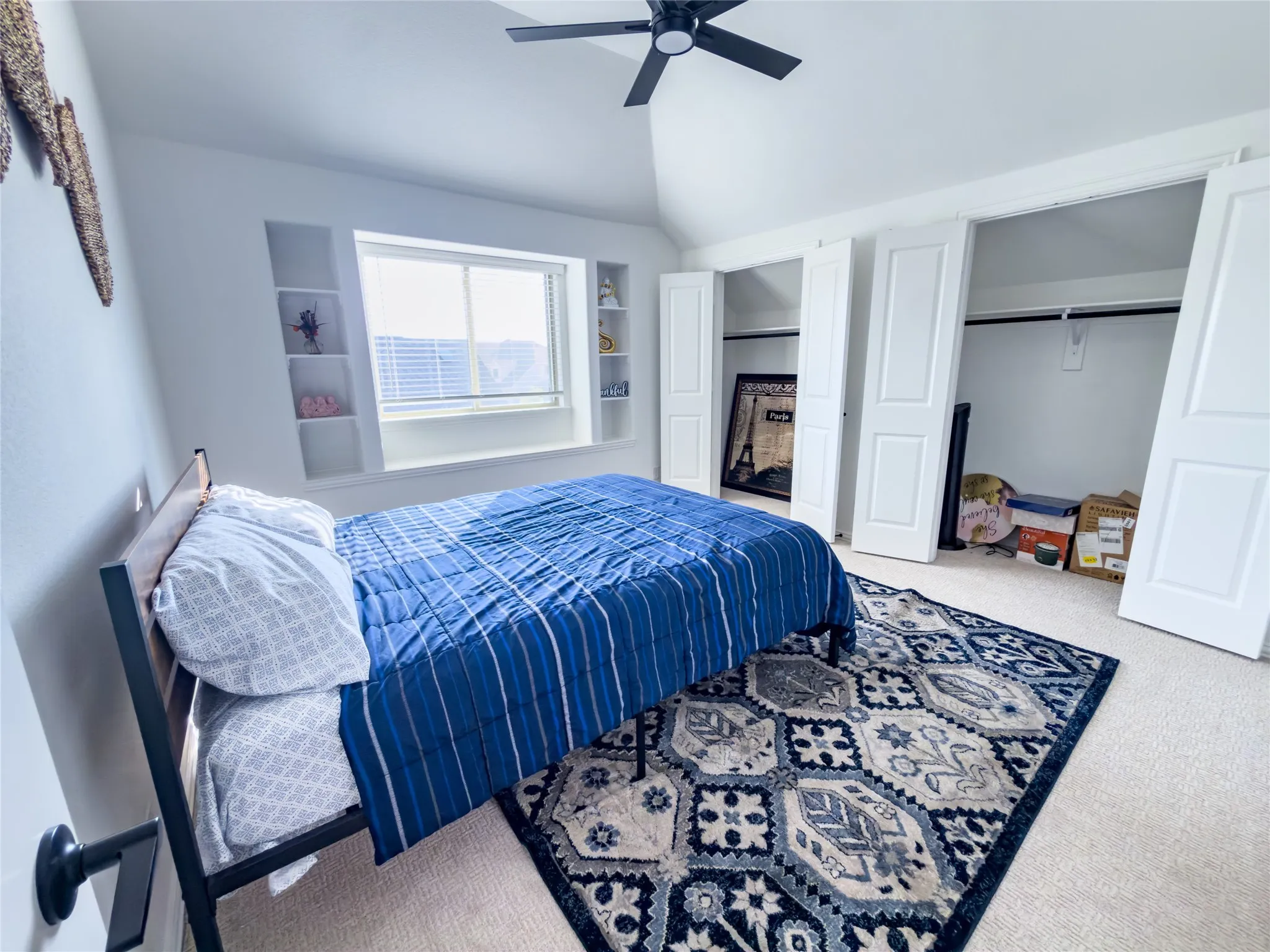 Carpeted bedroom with ceiling fan, vaulted ceiling, and multiple closets