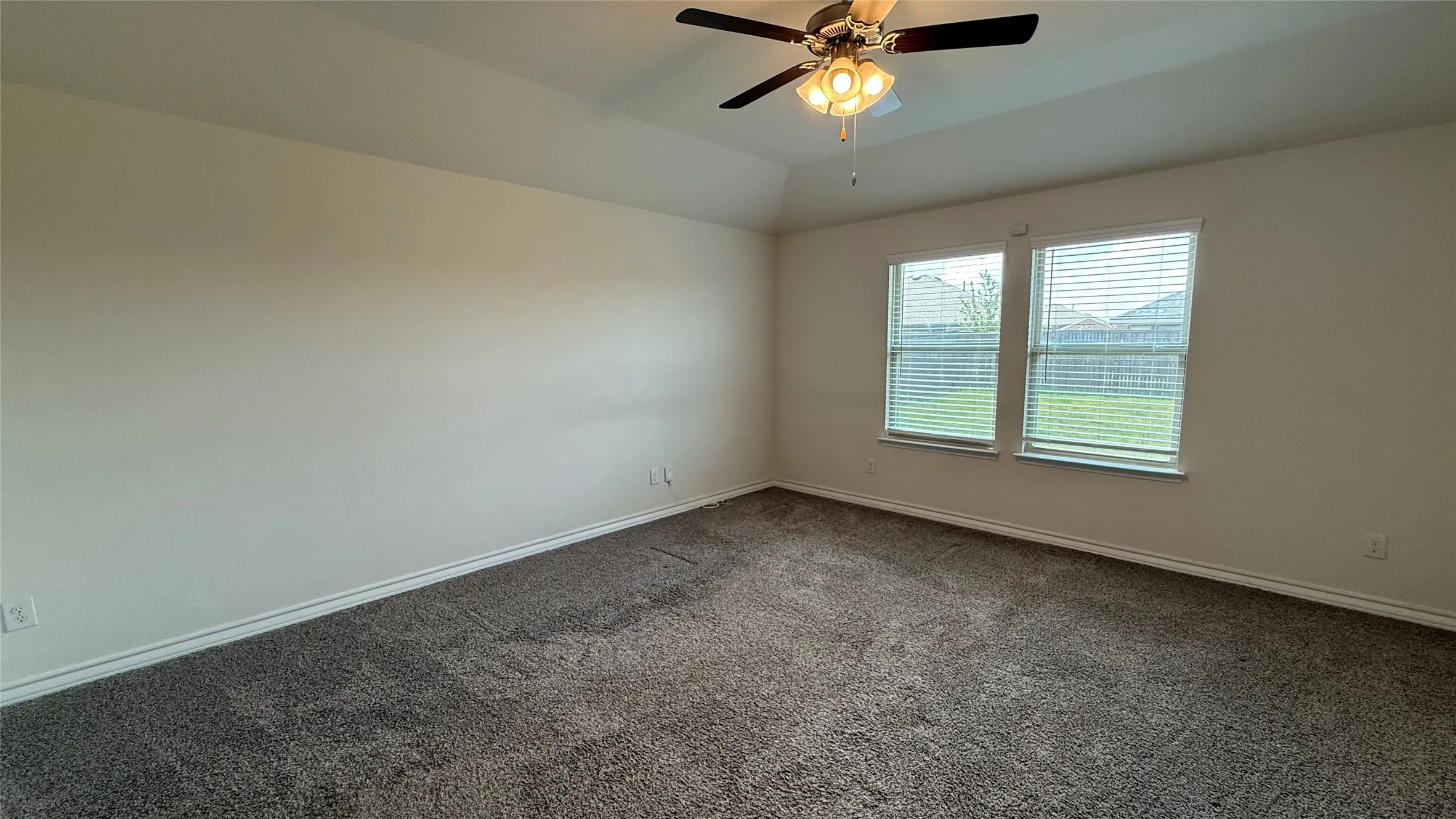 Vaulted ceiling with a ceiling fan, dual windows with blinds, and neutral carpeting