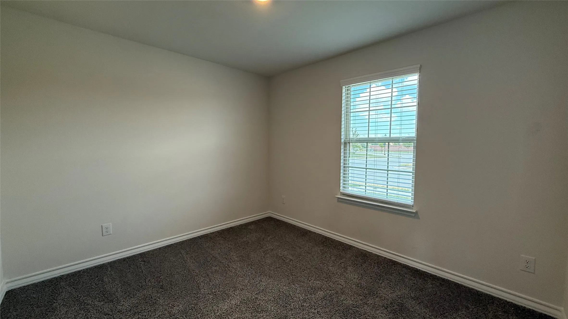 Neutral tone wall paint, dark grey carpeting, and a window with blinds