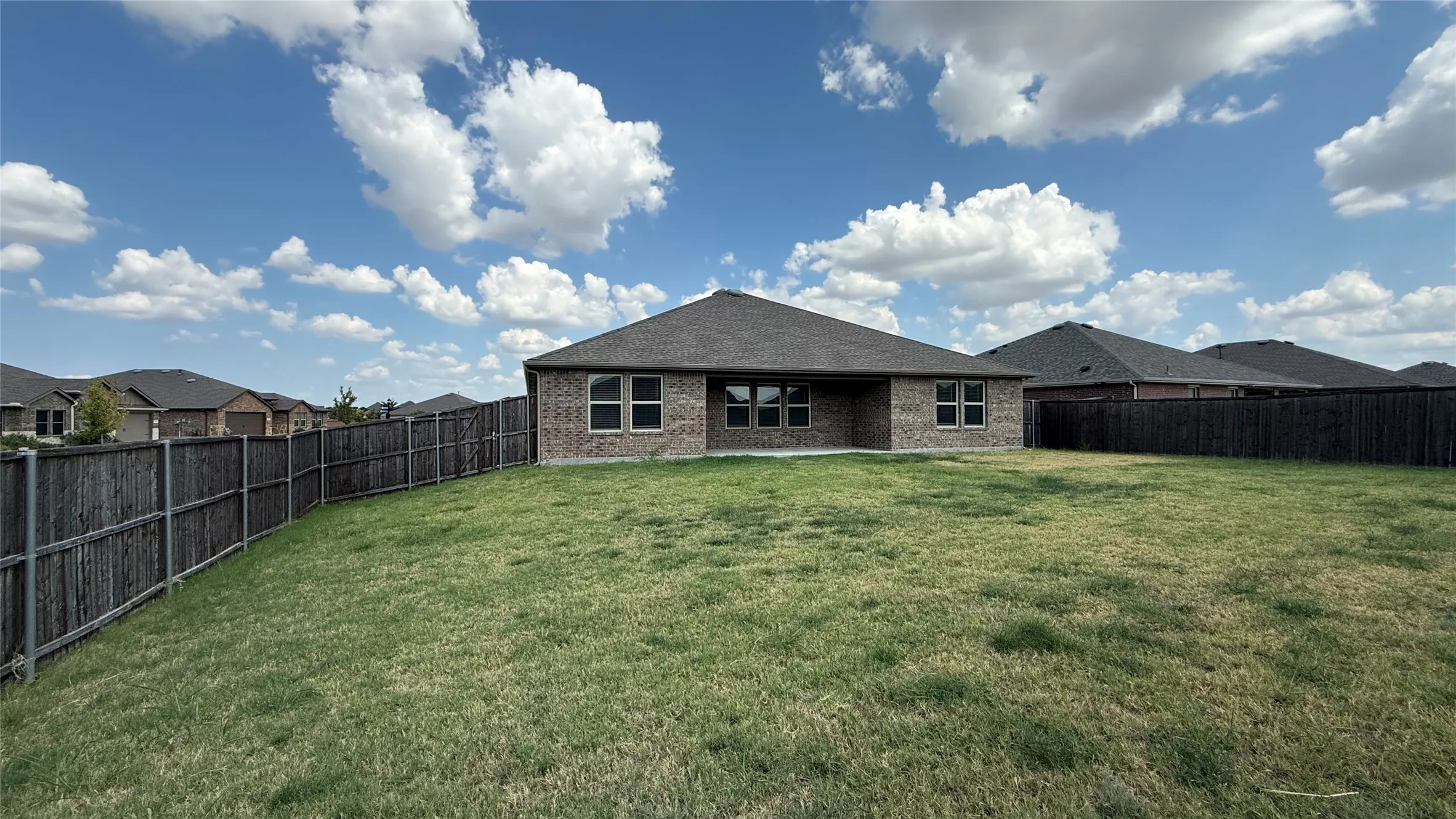 Expansive backyard featuring a manicured lawn, full perimeter privacy fencing, and a brick exterior